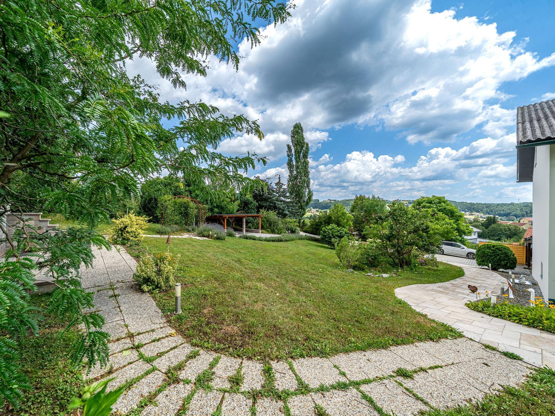 Weitläufiger Garten mit gepflastertem Weg und Blick auf das Haus sowie die umliegende Landschaft.
