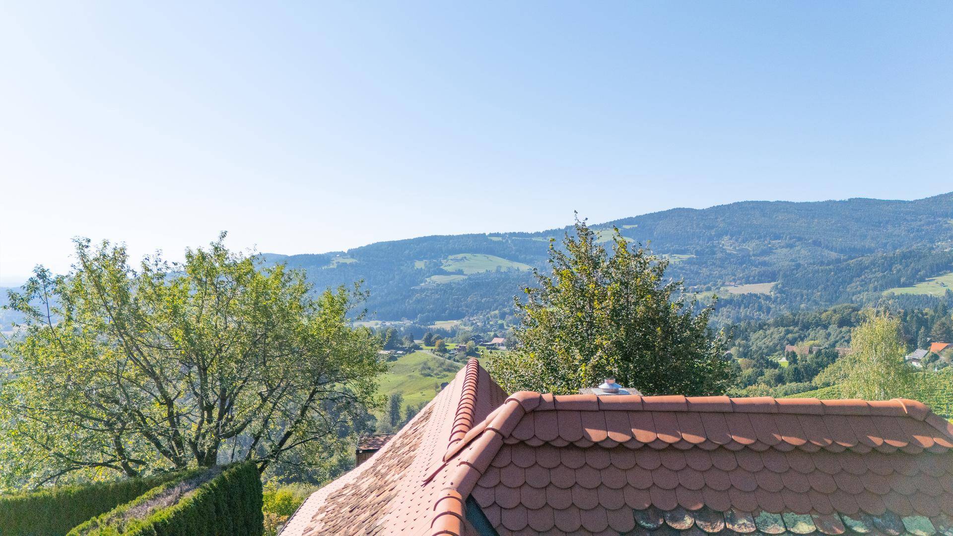 Ausblick über ein Ziegeldach auf die umliegenden grünen Hügel und Wälder.