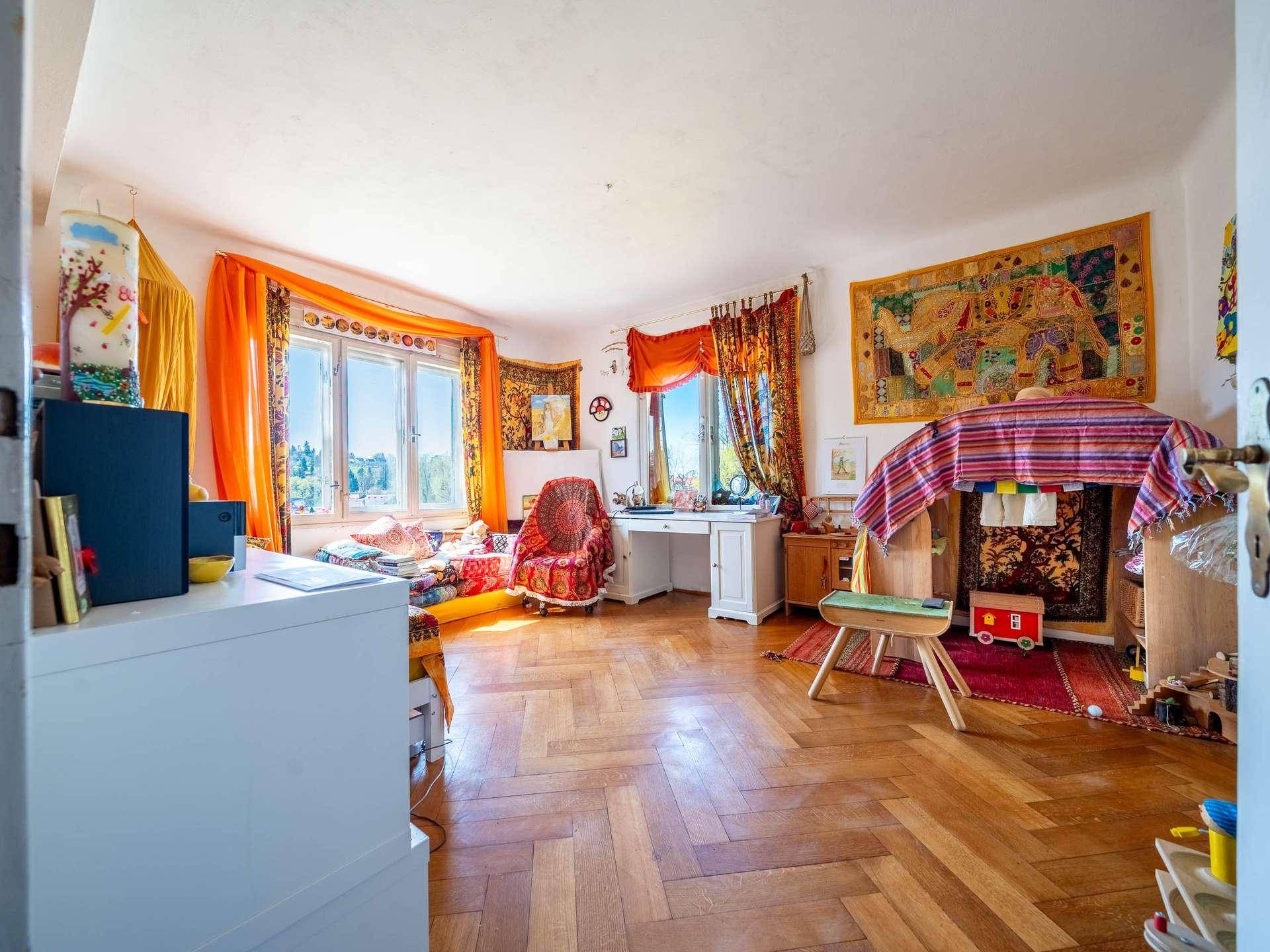 Geräumiges Wohnzimmer mit Parkettboden, großen Fenstern und farbenfroher Einrichtung.