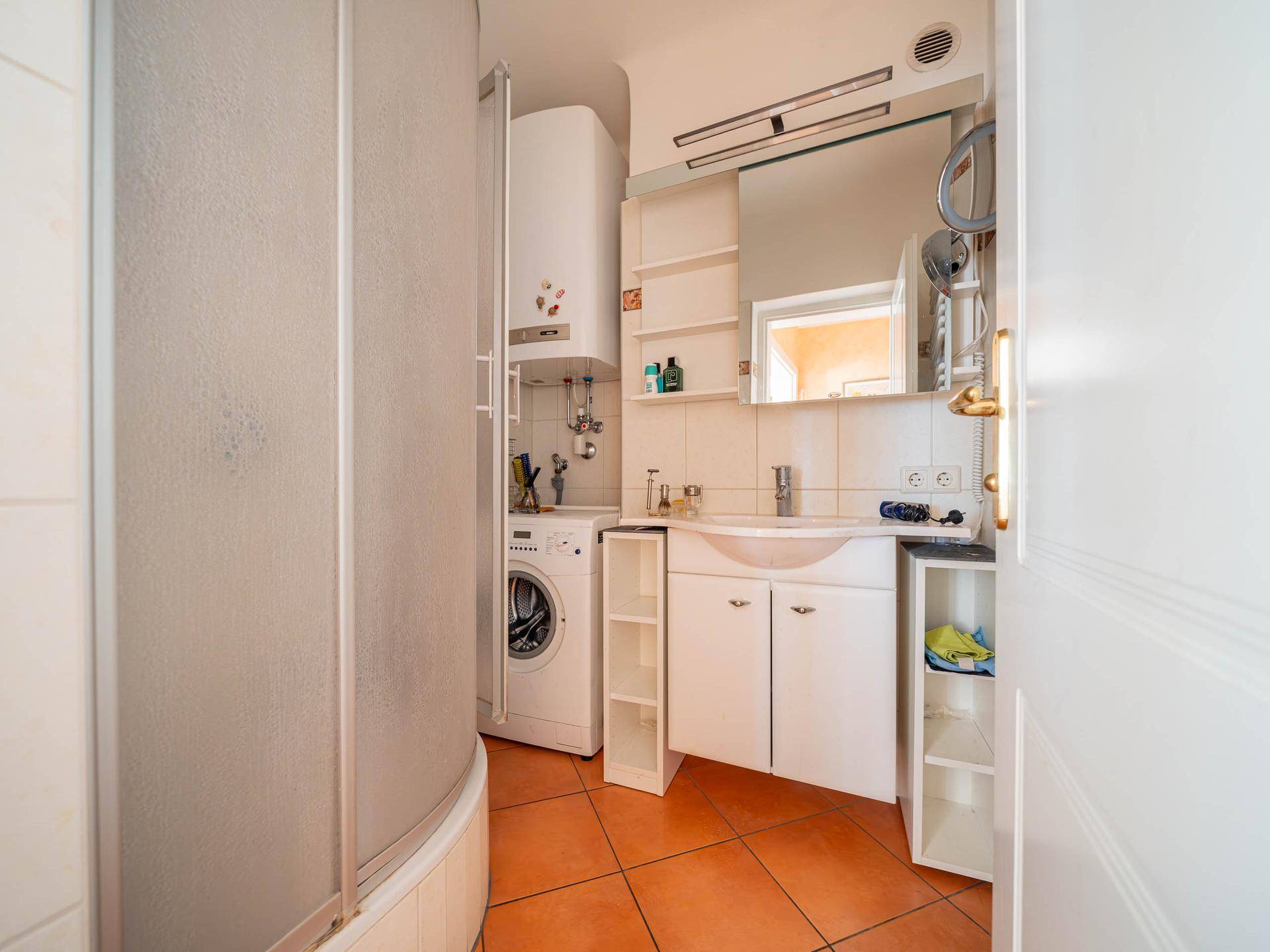 Badezimmer mit Dusche, Waschmaschine und Waschbecken mit Spiegelschrank.