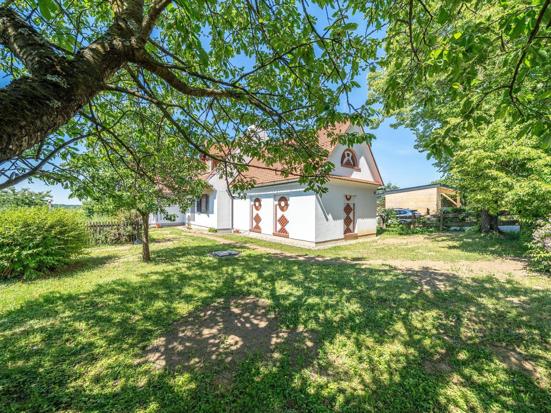 Gepflegter Gartenbereich mit Rasenfläche und schattenspendenden Bäumen neben dem Haus.
