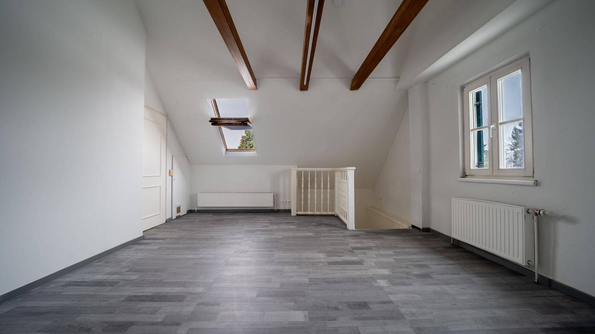 Helles Dachzimmer mit Holzbalken, Dachfenster und großem Fenster, das viel Licht spendet.