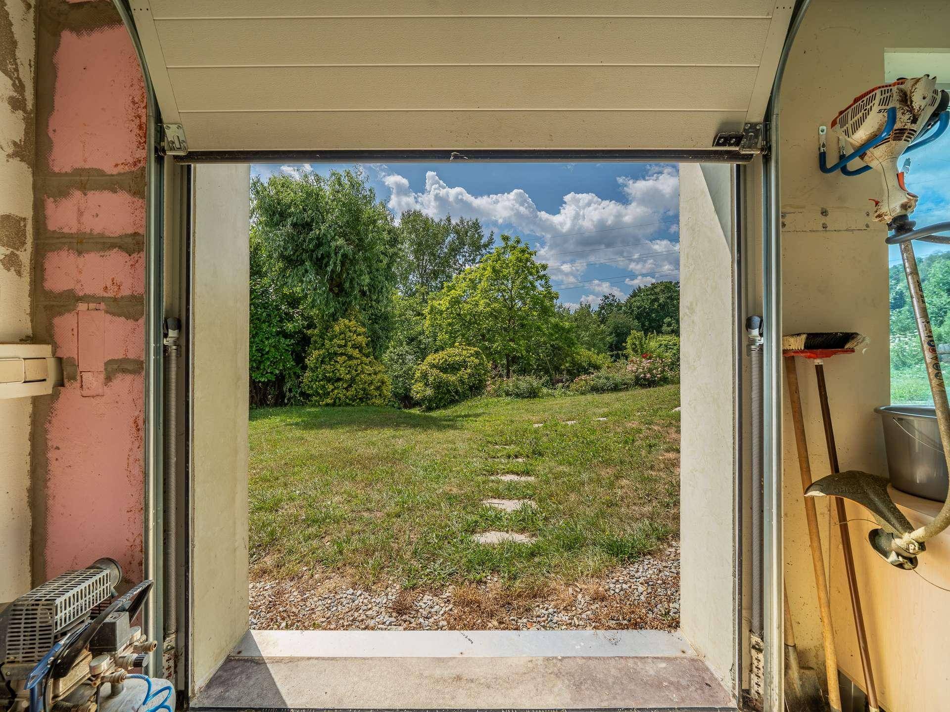 Blick aus der Garage in den gepflegten Garten mit Rasenfläche und Bäumen.