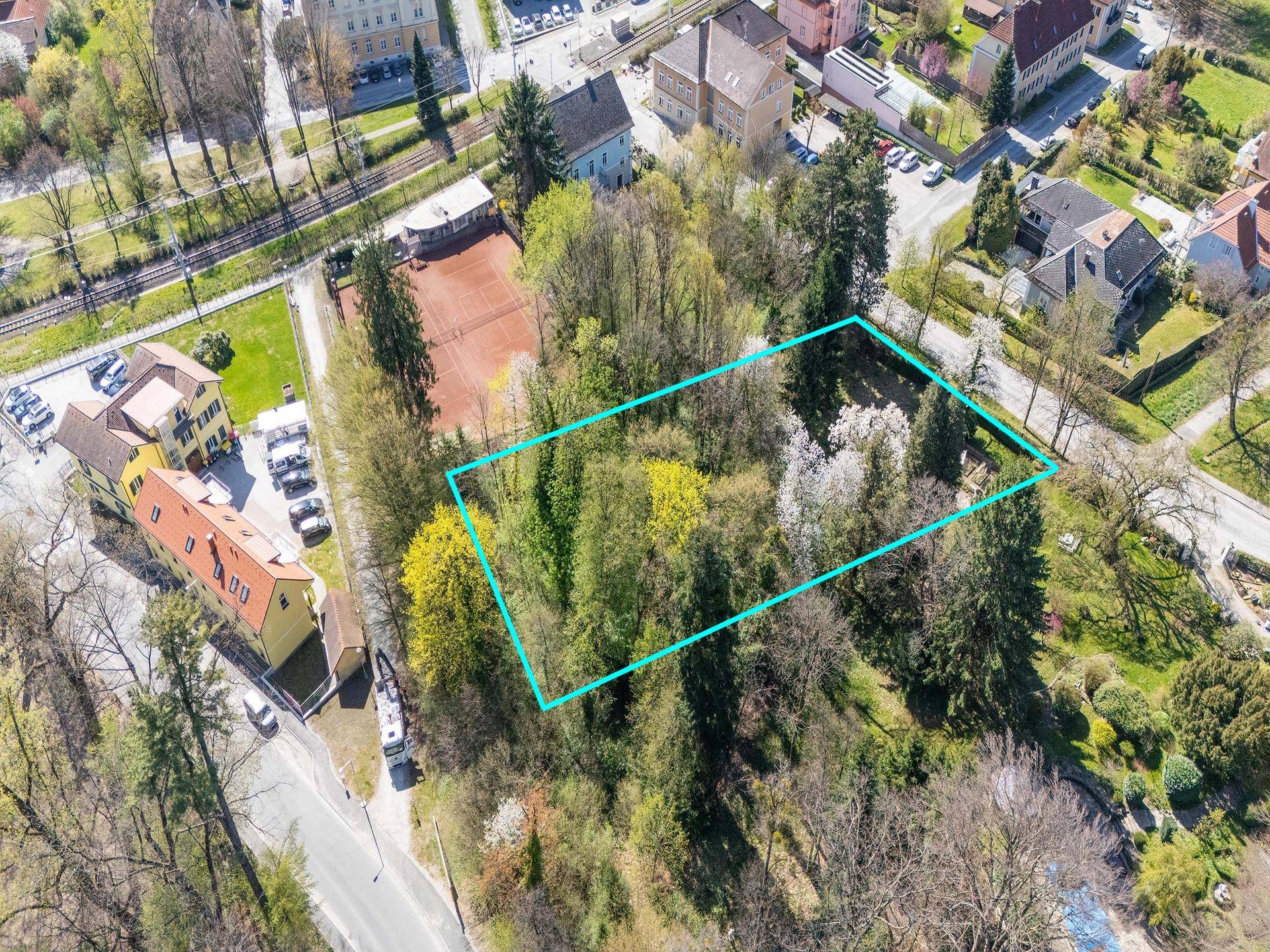 Vogelperspektive auf das bewaldete Grundstück mit blauer Markierung, angrenzend an einen Tennisplatz.