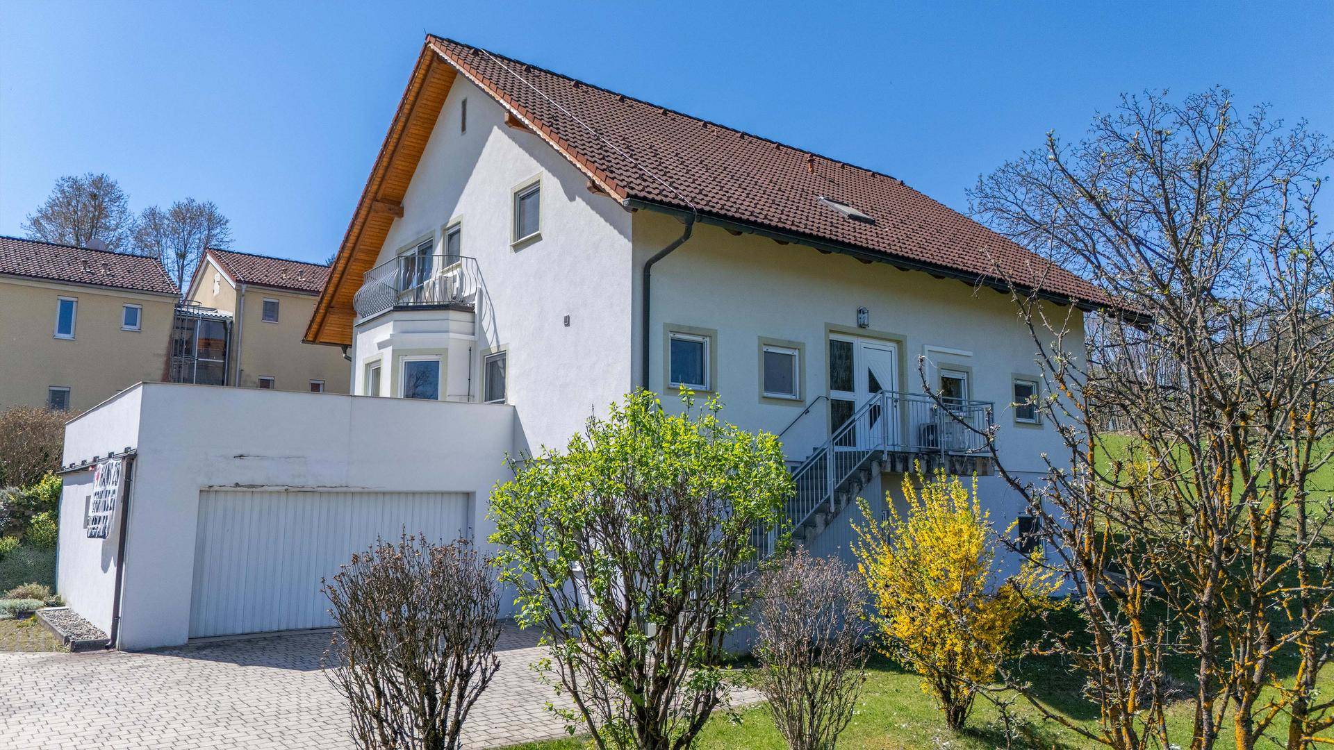 Ansicht des Einfamilienhauses mit Garage und Zugangstreppe, umgeben von grüner Landschaft.