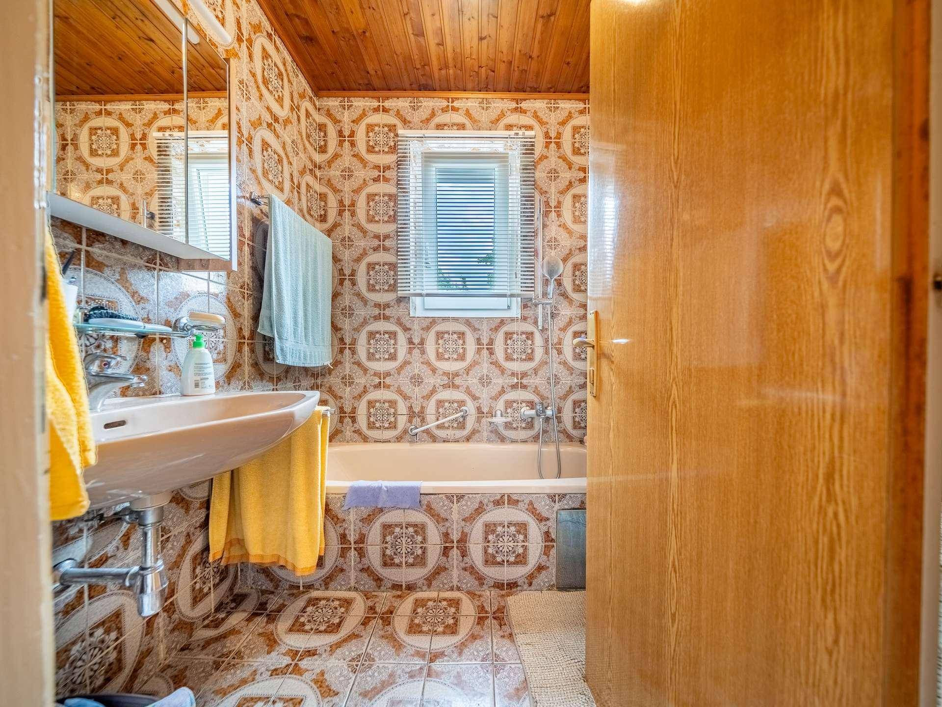 Badezimmer im 80er-Jahre-Stil mit Badewanne, Waschbecken und gemusterten Fliesen.