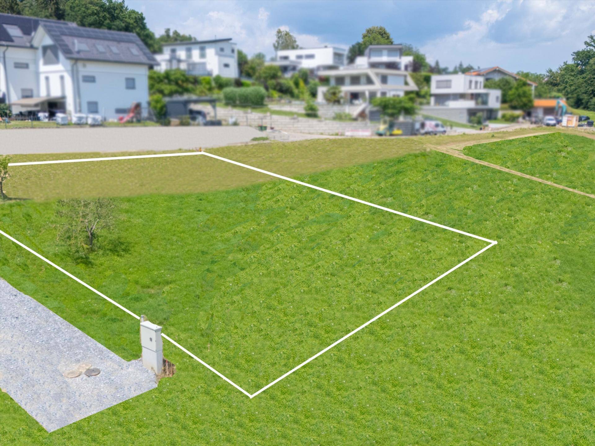 Luftaufnahme eines grünen Grundstücks mit markierten Grenzen und modernen Häusern im Hintergrund.