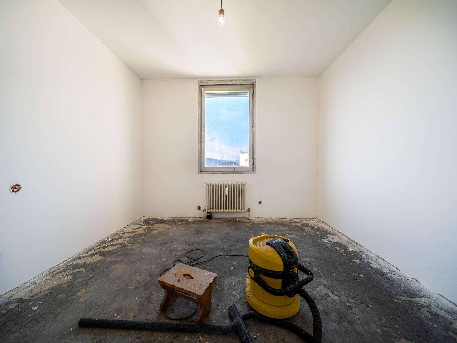 Leeres Zimmer in Renovierung mit Fenster, Heizkörper und Reinigungsgeräten für den Umbau.