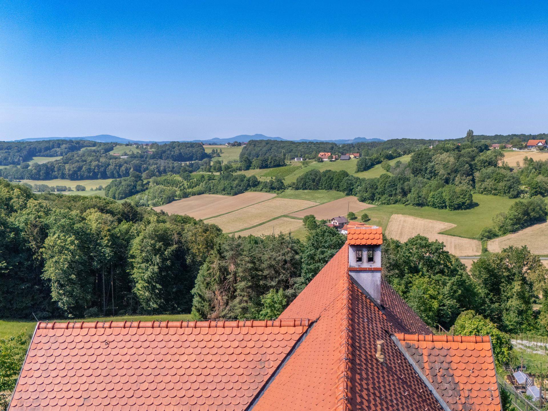Weitblick über das rote Ziegeldach des Hauses auf eine hügelige, grüne Landschaft.