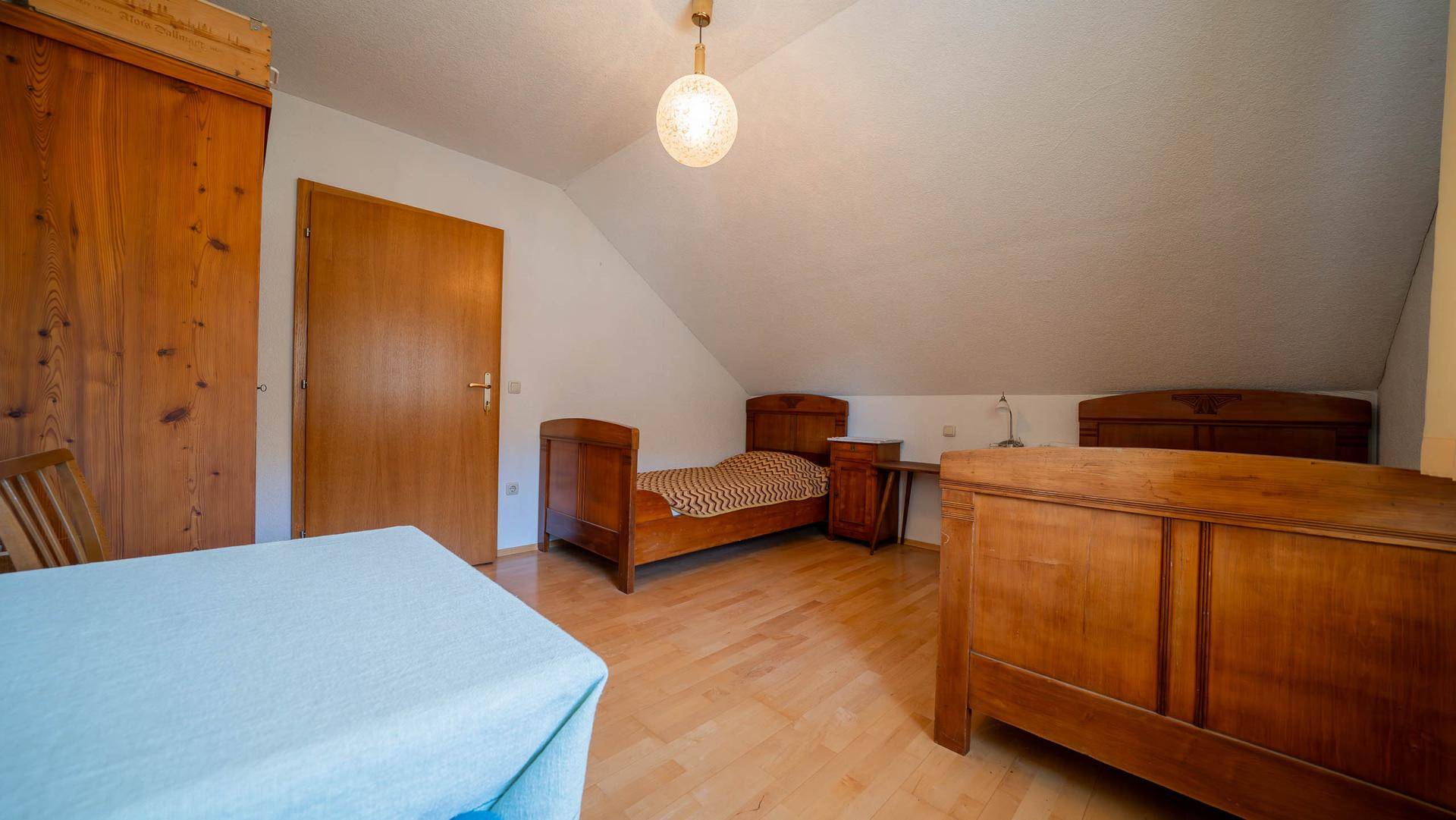 Schlafzimmer im Dachgeschoss mit Holzboden, Dachschräge und traditionellen Holzmöbeln.