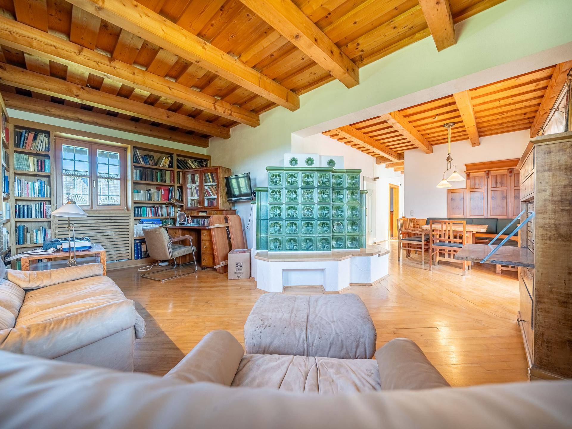 Gemütliches Wohnzimmer mit Holzbalkendecke, Kachelofen und umfangreicher Bibliothek.
