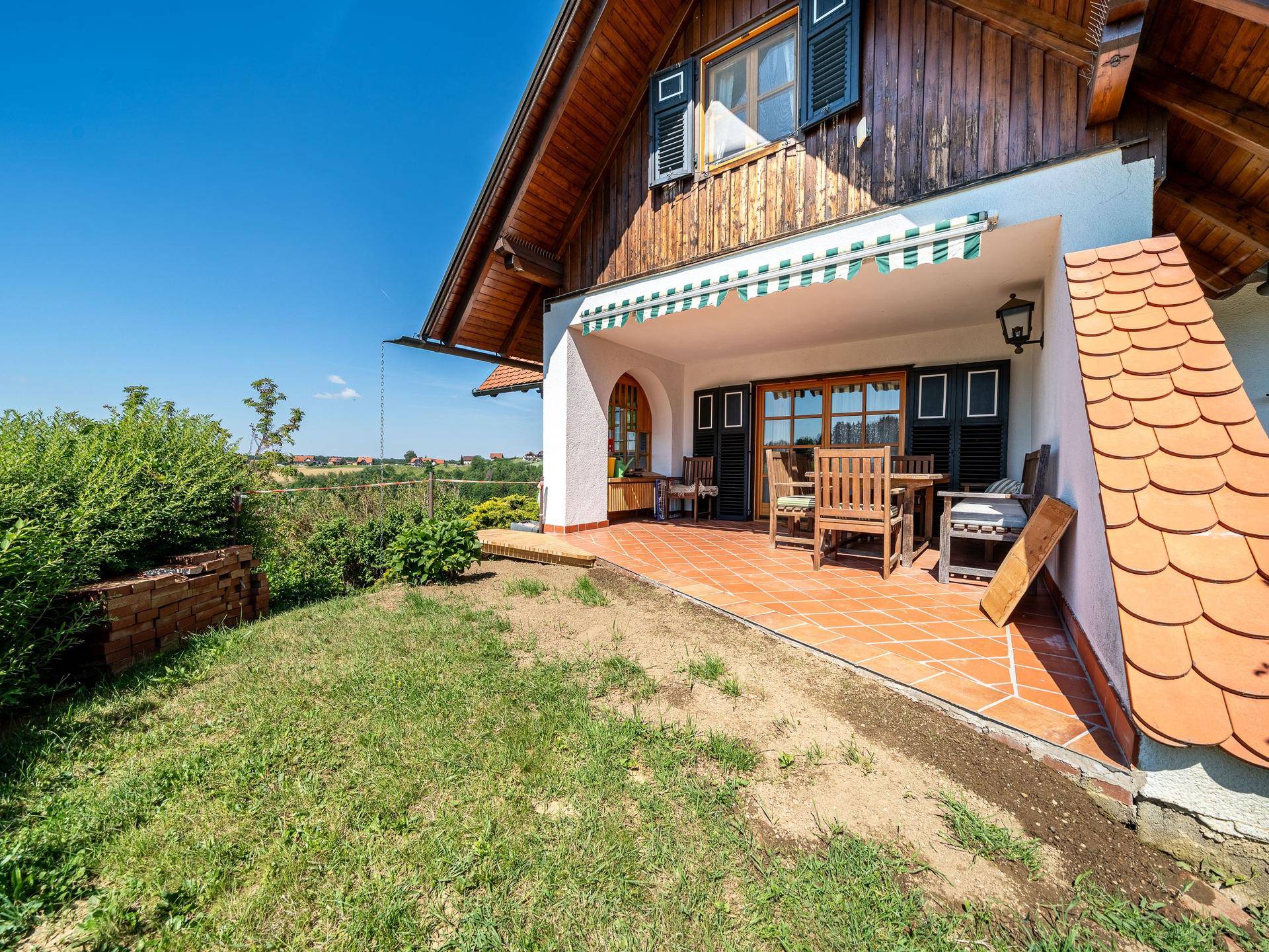 Sonniger Terrassenbereich mit Gartenmöbeln, angrenzendem Rasen und Blick auf die Landschaft.