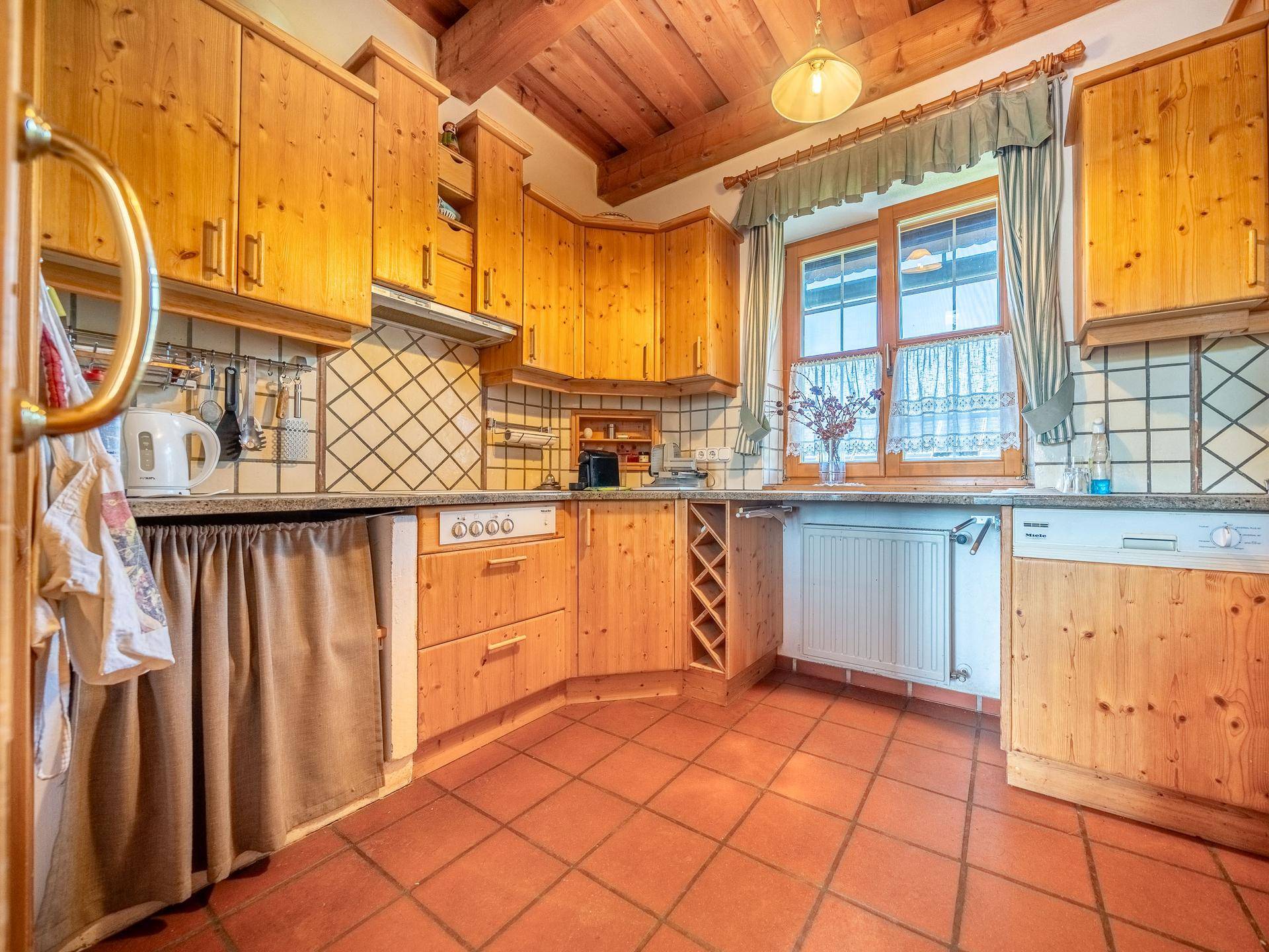 Traditionelle Holzküche mit Terrakotta-Fliesen, Einbaugeräten und Fenster mit Blick ins Grüne.