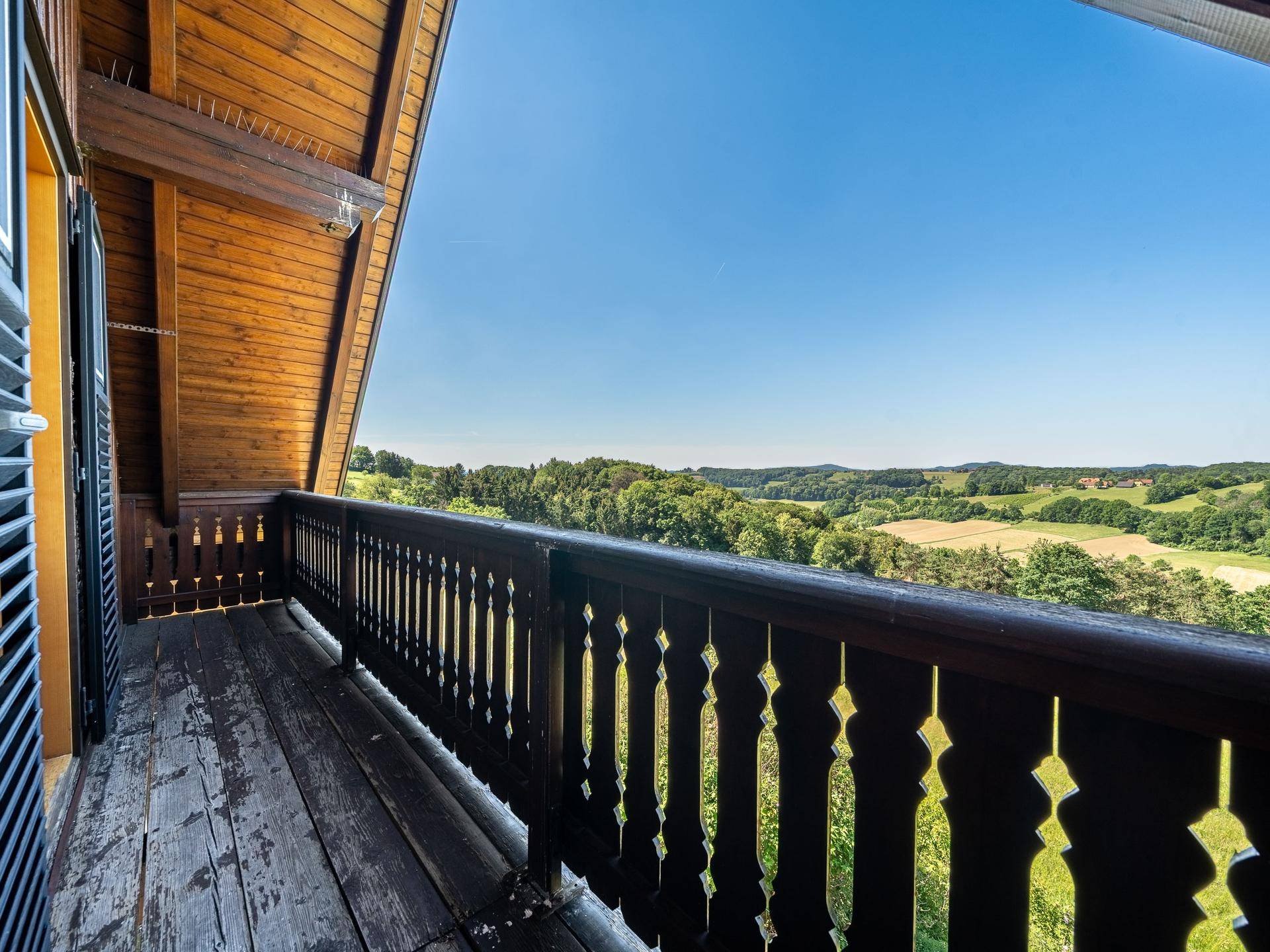 Traditioneller Holzbalkon mit geschnitztem Geländer und weitem Blick über die grüne Landschaft.