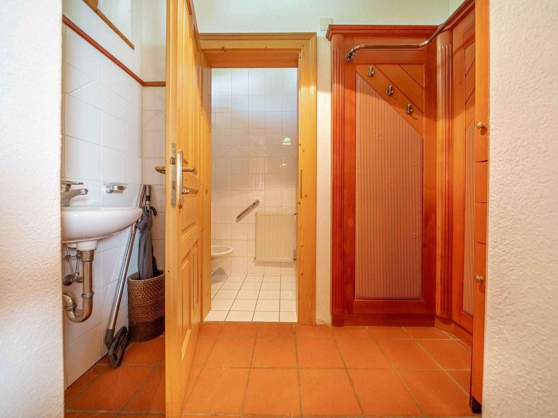 Kleines Gäste-WC mit weißen Fliesen, Waschbecken und Holztür im Landhausstil.
