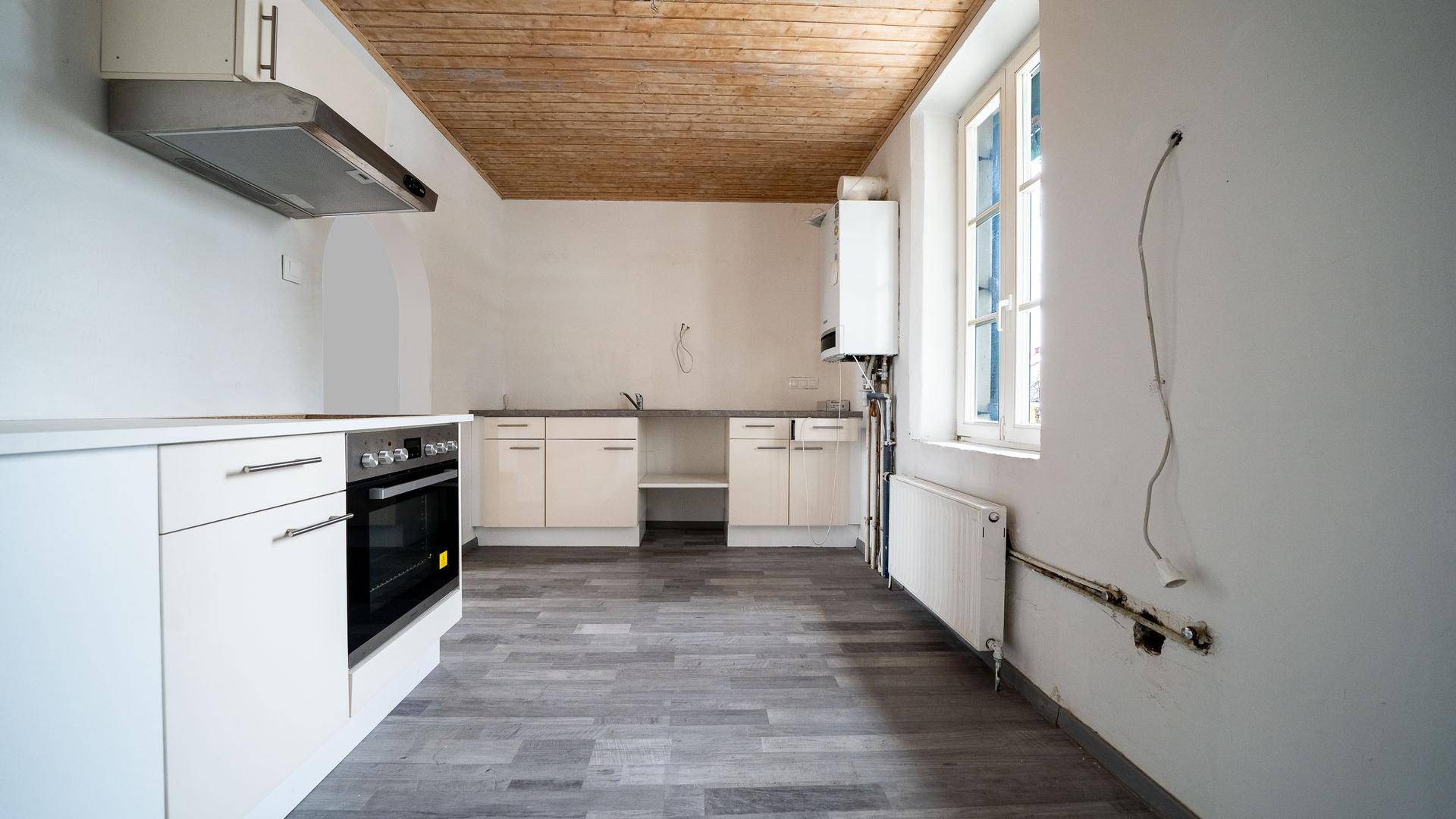Geräumige Küche mit weißen Unterschränken, Heizkörper und Fenster, bereit für die Installation der Spüle.