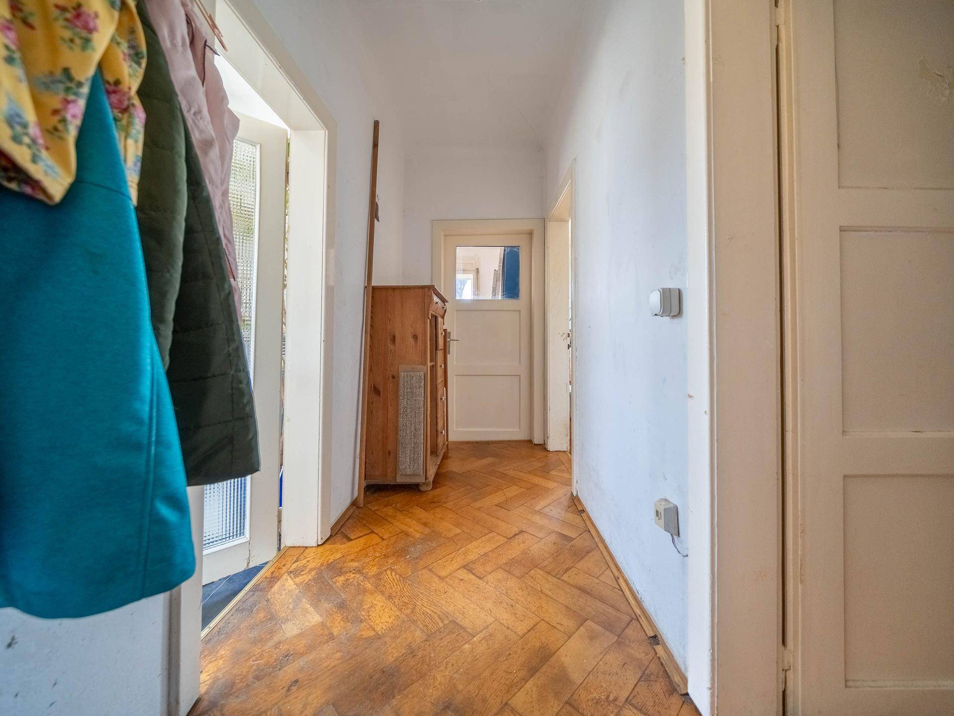 Flur mit Fischgrätparkett und Garderobe, der zu verschiedenen Zimmern führt.