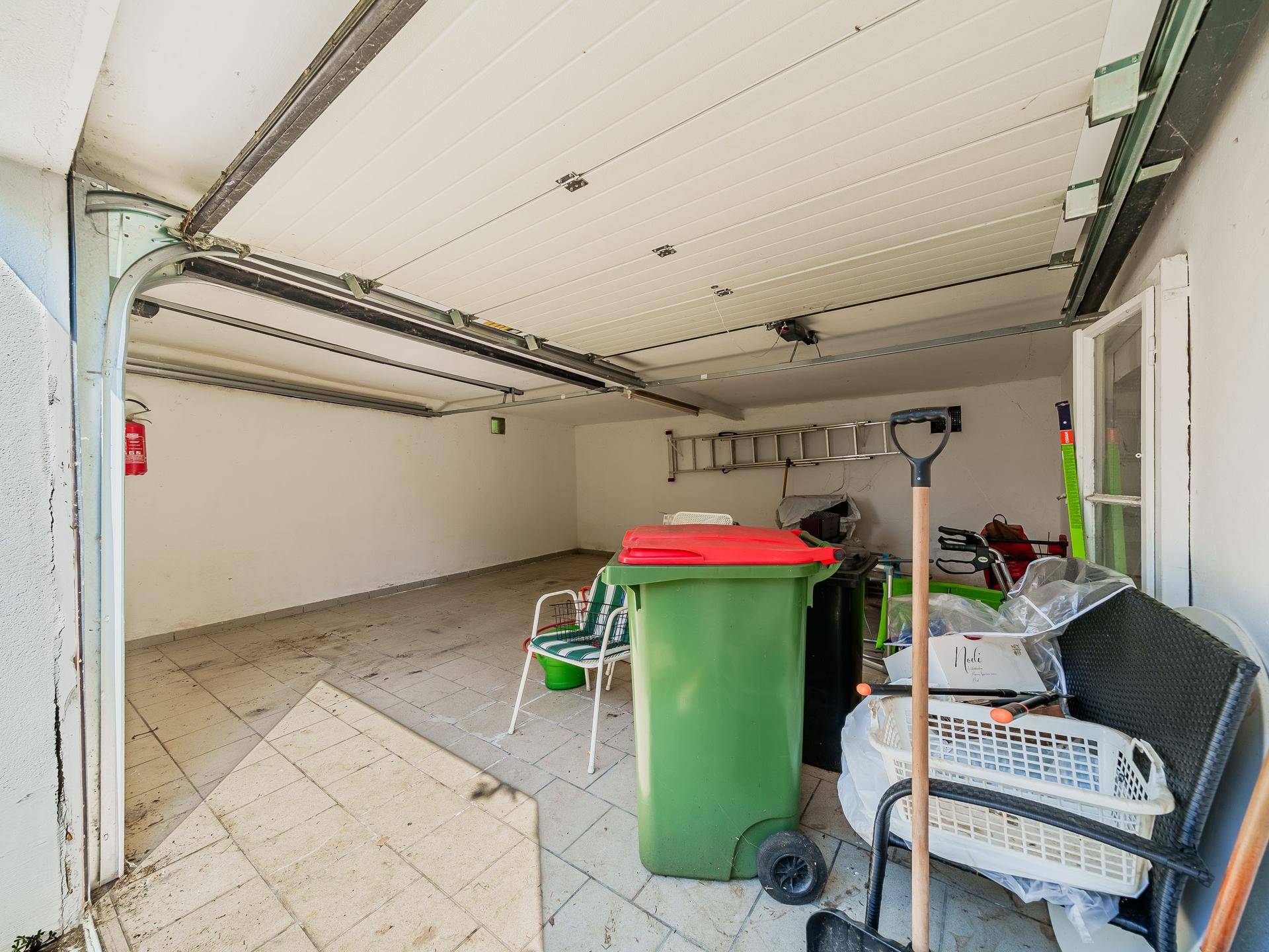 Innenansicht der Garage mit Fliesenboden, offenem Tor und Abstellmöglichkeiten.