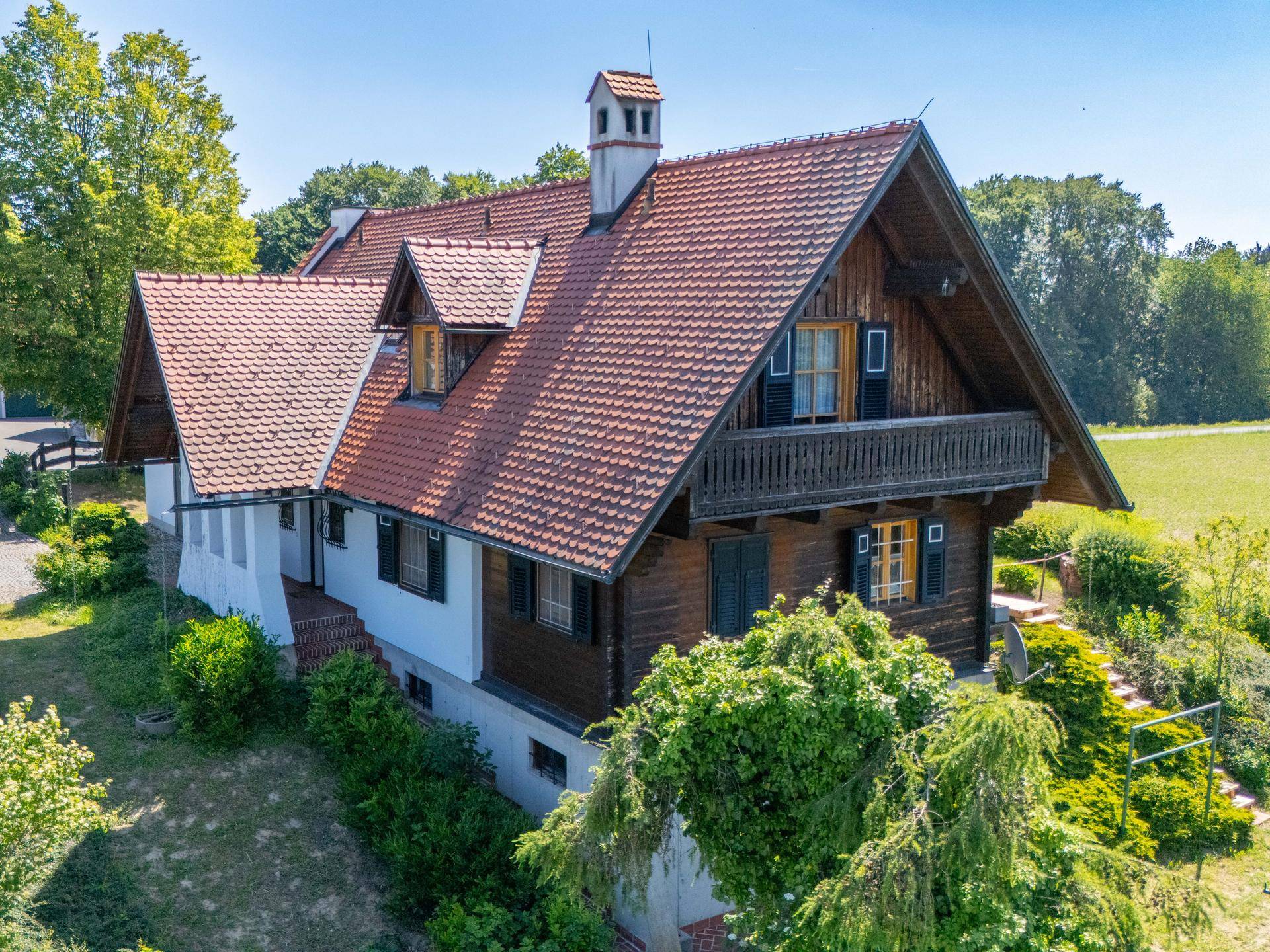 Seitenansicht des Hauses mit Holzfassade, traditionellem Balkon und grüner Umgebung.