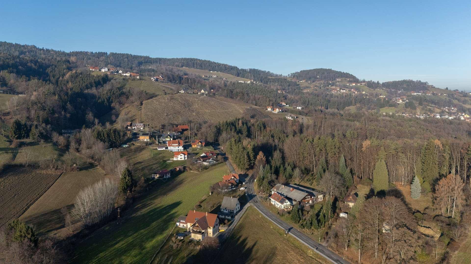 Panoramablick auf ein Dorf in einem Tal, umgeben von Wäldern und sanften Hügeln.