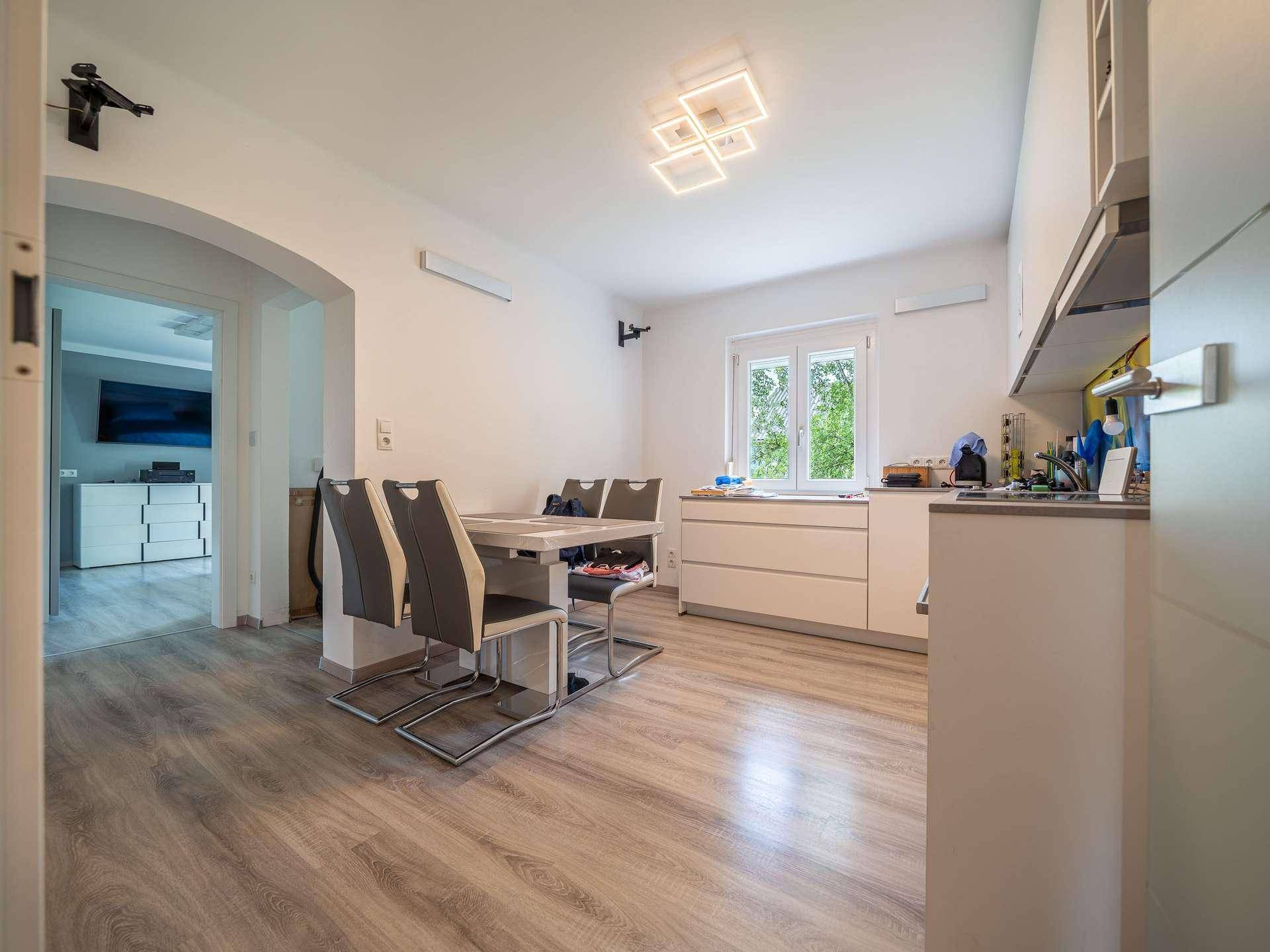 Moderne Küche mit Essbereich, hellen Schränken und Laminatboden.