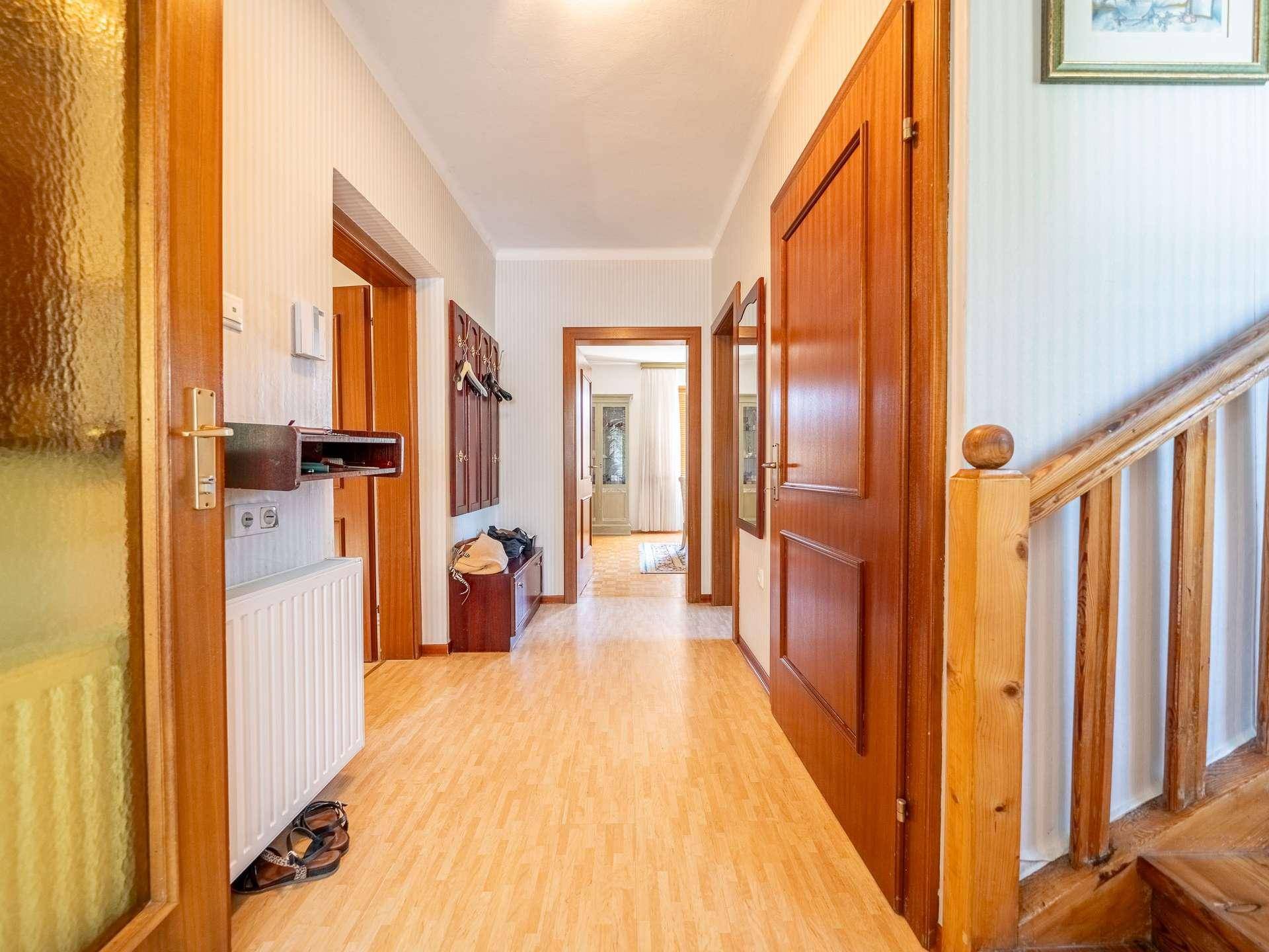 Heller Flur mit Laminatboden und einer Holztreppe, die zu den oberen Etagen führt.