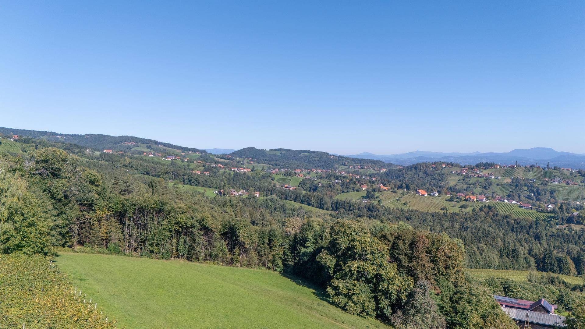 Weites Panorama über grüne Hügel, Wälder und ländliche Siedlungen unter blauem Himmel.