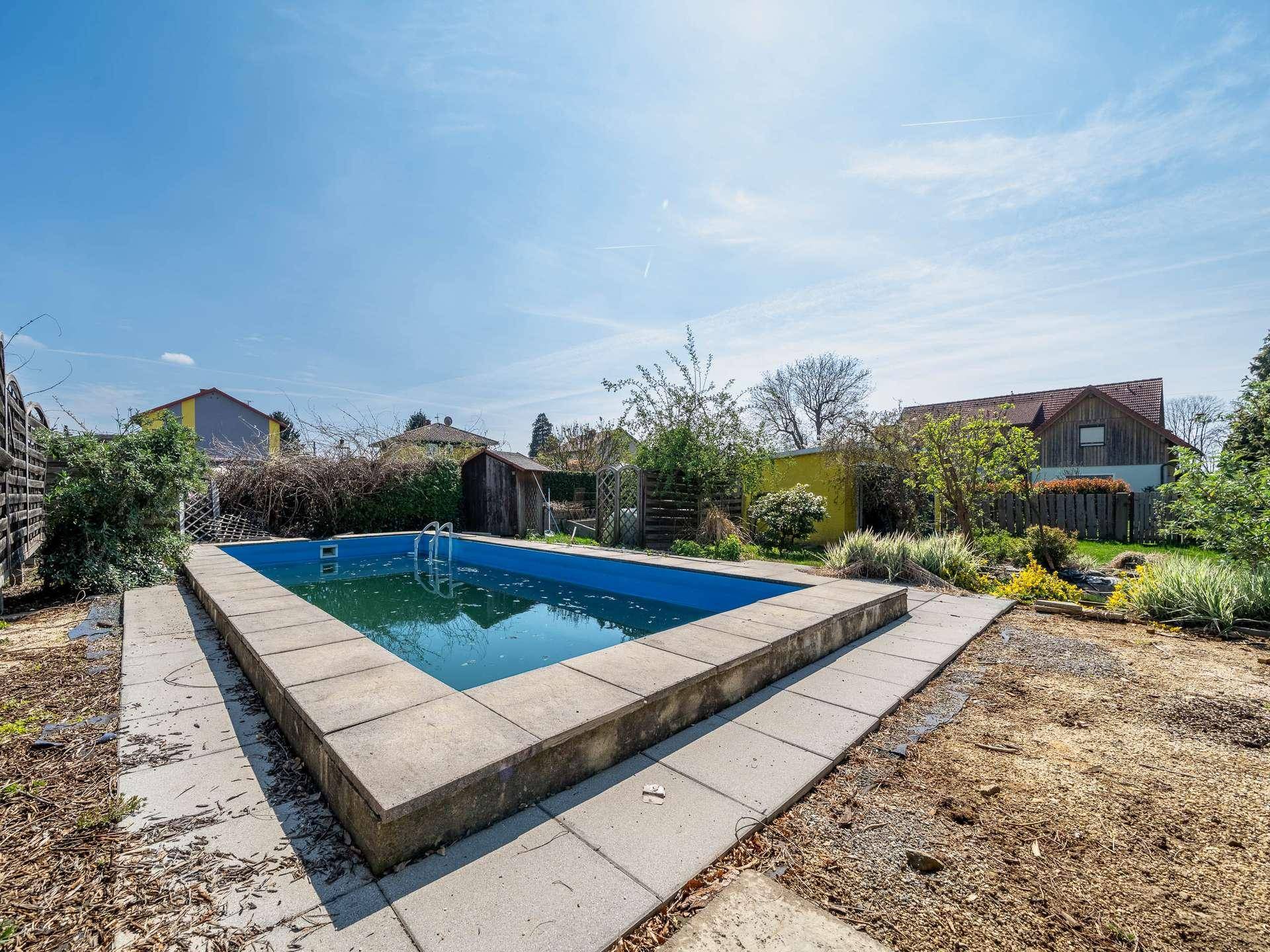 Außenpool im Gartenbereich mit gepflasterter Umrandung unter blauem Himmel.