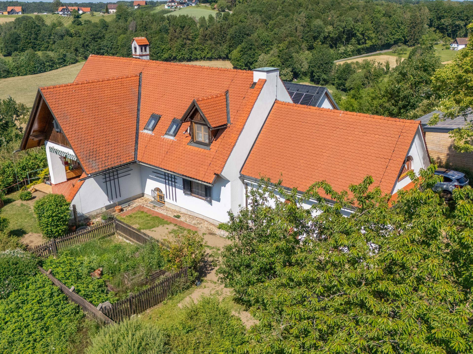 Vogelperspektive eines Einfamilienhauses mit rotem Ziegeldach und umgebender grüner Landschaft.