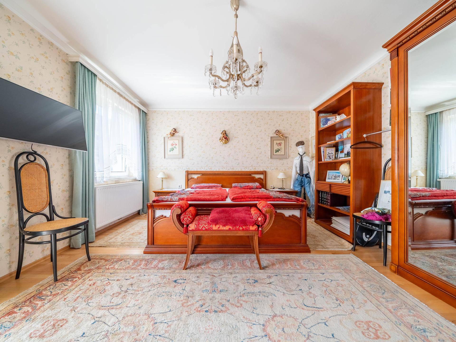 Helles Schlafzimmer mit Holzbett, Teppich und Kronleuchter.