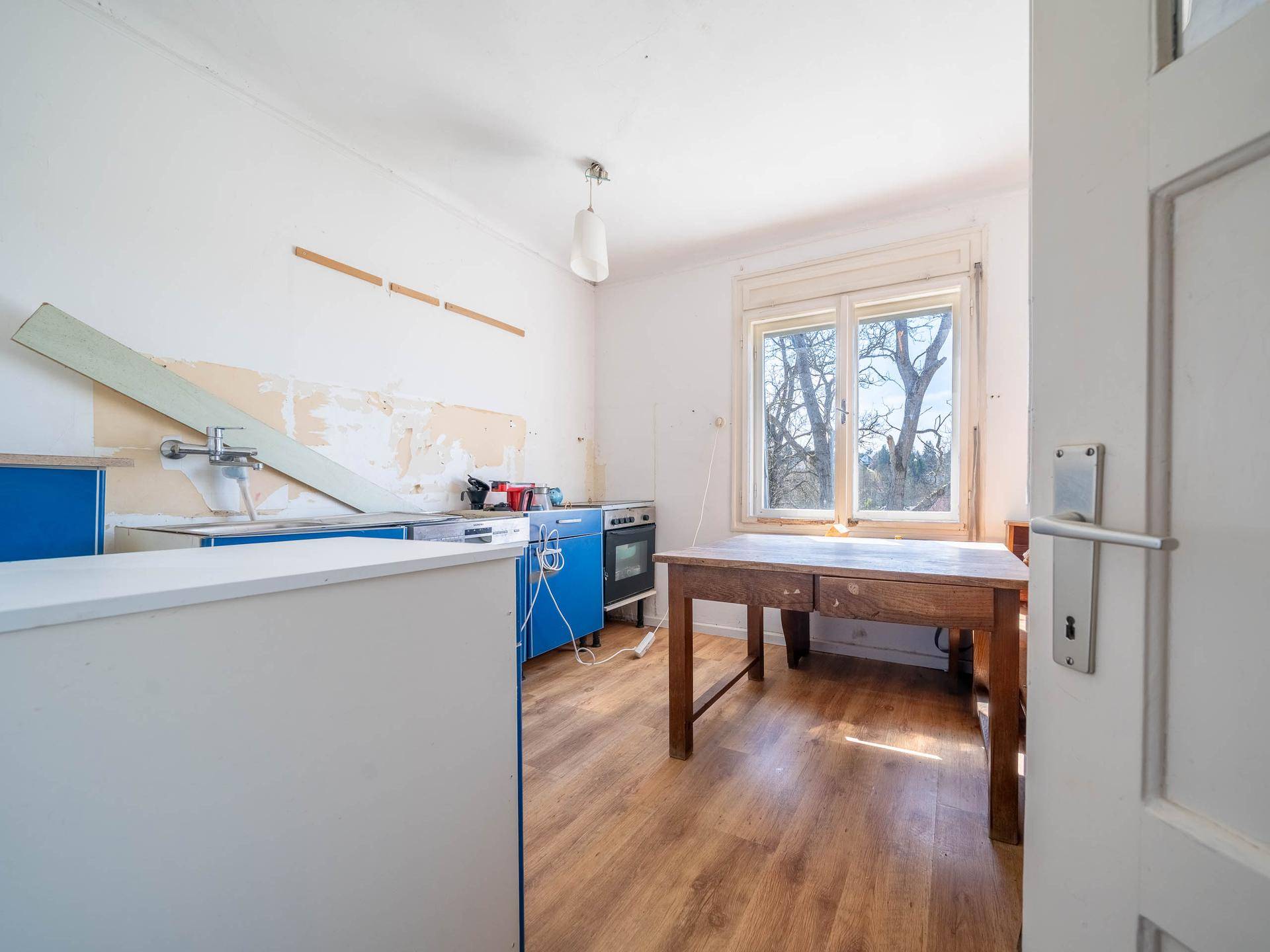 Küche in Renovierung mit blauen Unterschränken, Holztisch und Fenster.