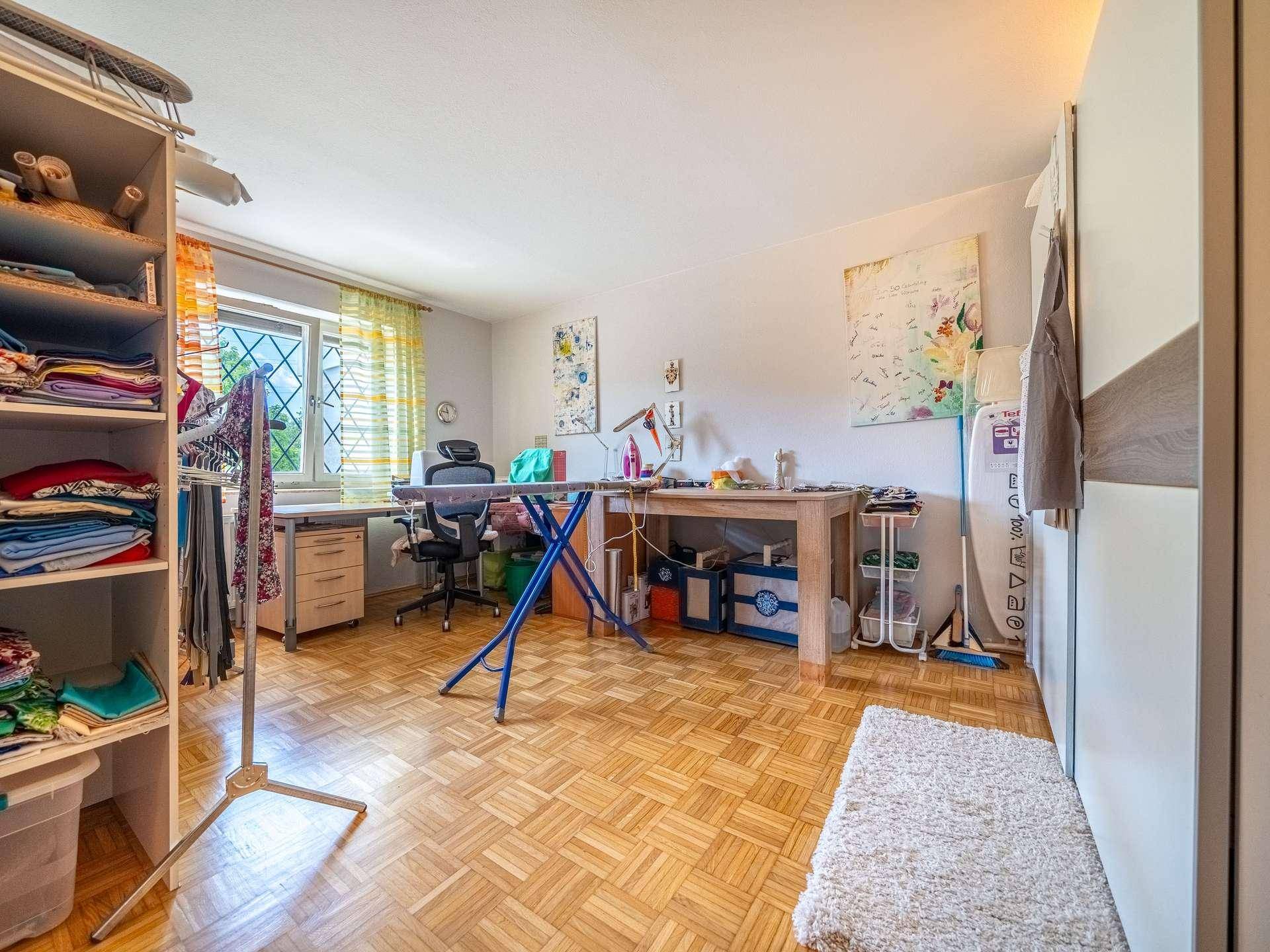 Helles Arbeitszimmer mit Parkettboden, großem Fenster und viel Platz für kreative Tätigkeiten.