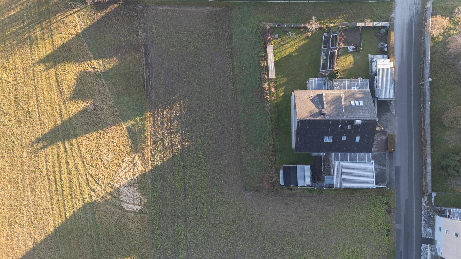 Senkrechte Luftaufnahme eines Hauses mit Garten und angrenzenden Feldern, lange Schatten deuten auf tiefstehende Sonne hin.