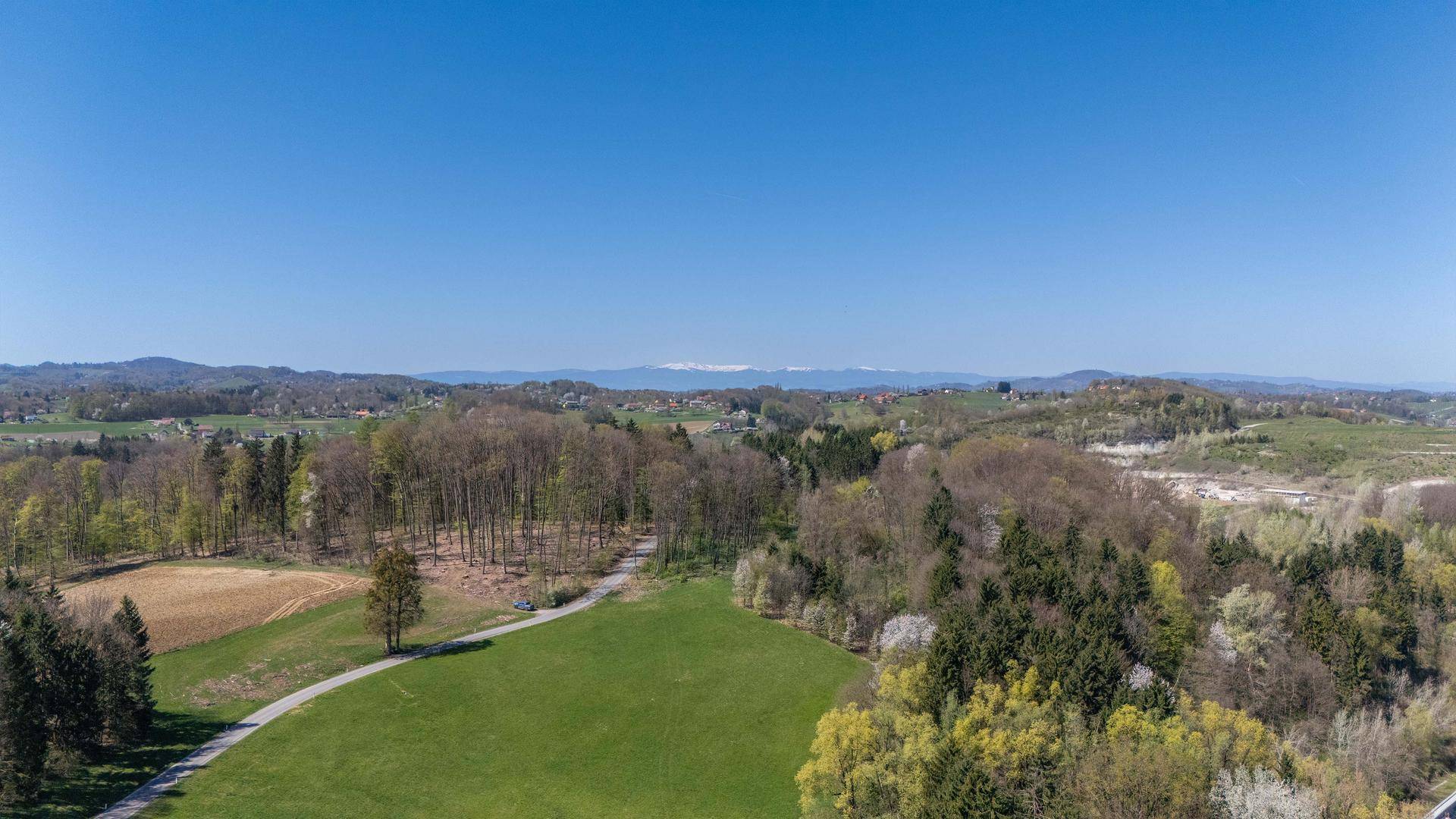 Weitläufige Landschaftsaufnahme mit Wäldern, Feldern und Bergen am Horizont unter blauem Himmel.