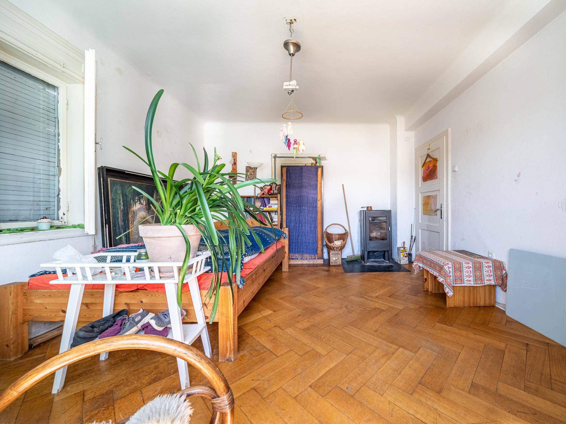 Helles Zimmer mit Parkettboden, Pflanzen und einem Holzofen als Heizquelle.