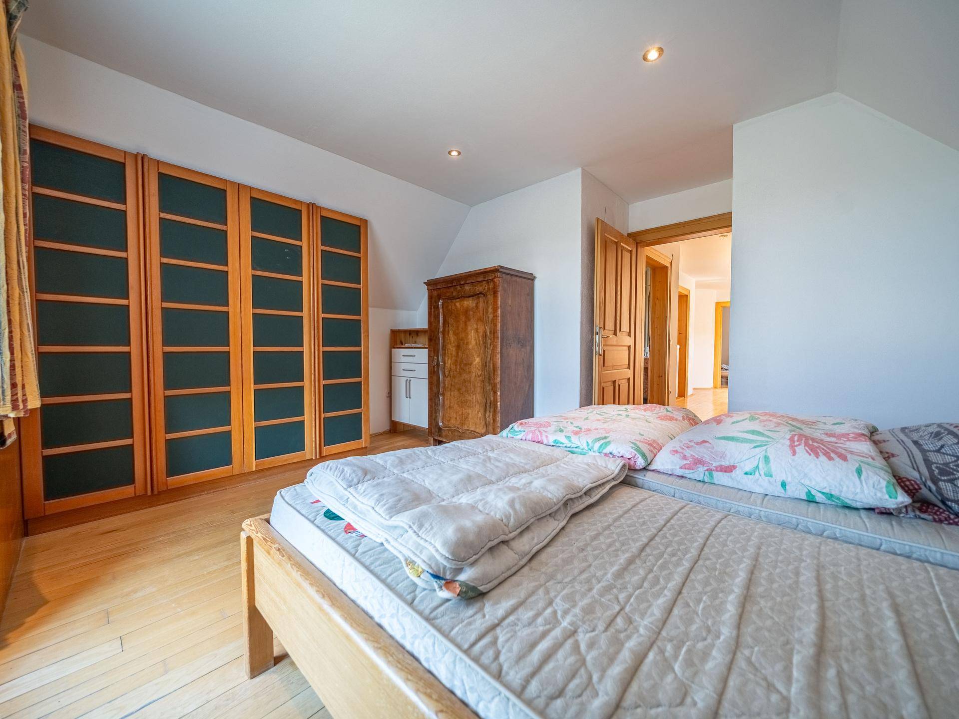 Schlafzimmer mit Holzbett, Einbauschränken und Zugang zu einem weiteren Raum im Dachgeschoss.
