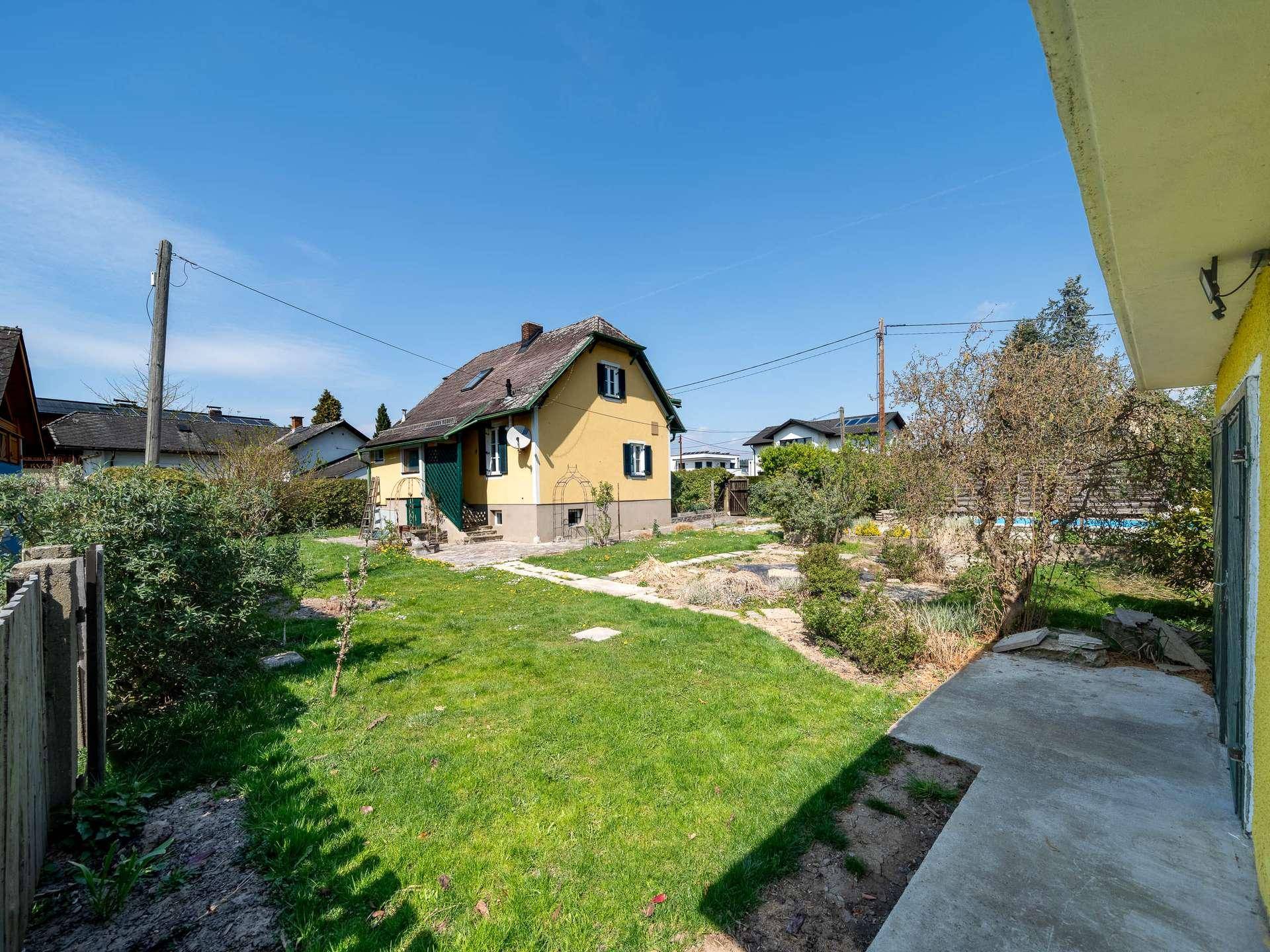 Großer Garten mit Rasenfläche, Bäumen und Blick auf das gelbe Einfamilienhaus.