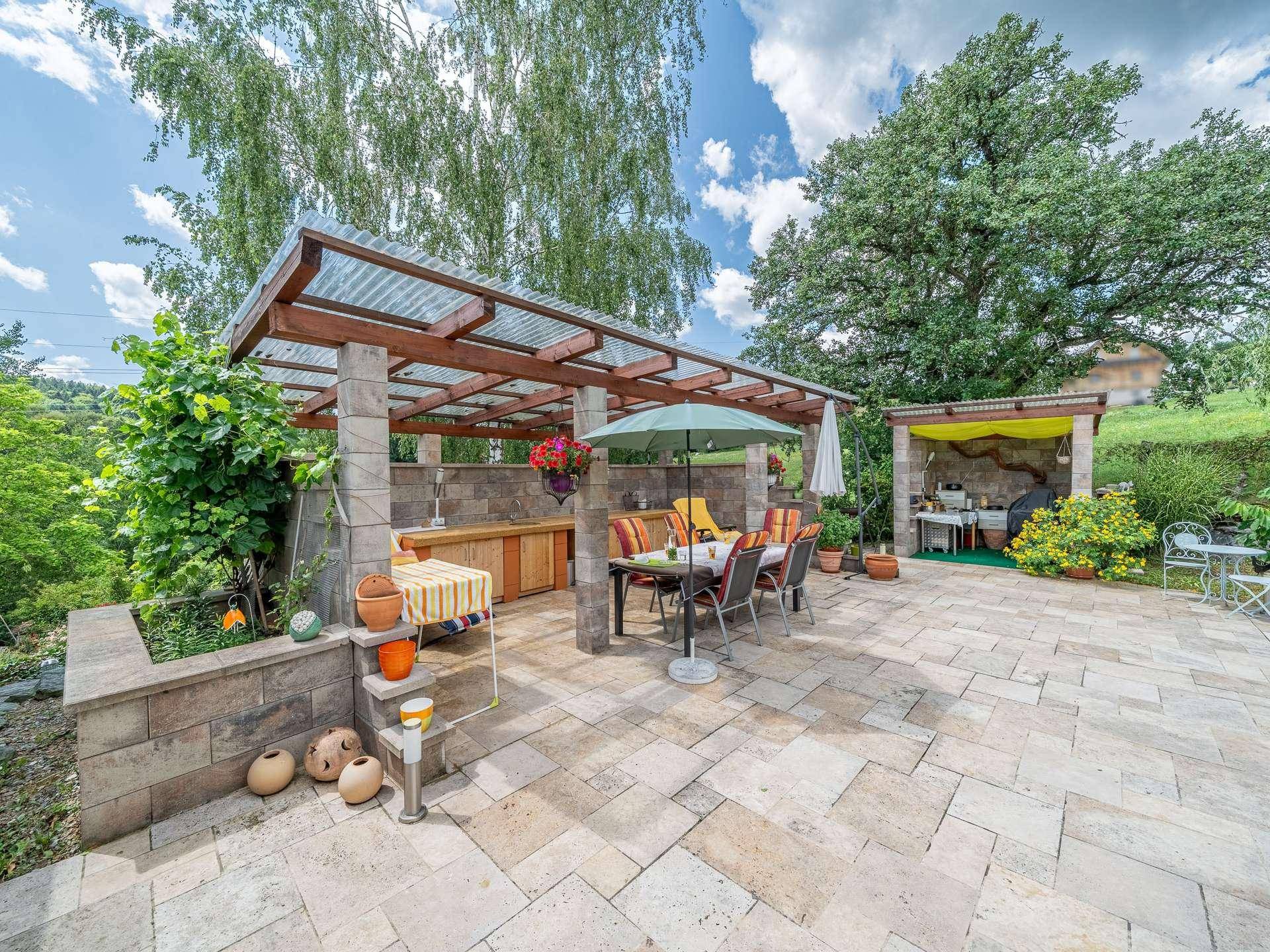 Geräumige, gepflasterte Terrasse mit überdachter Außenküche, Grillbereich und Essplatz im Freien.