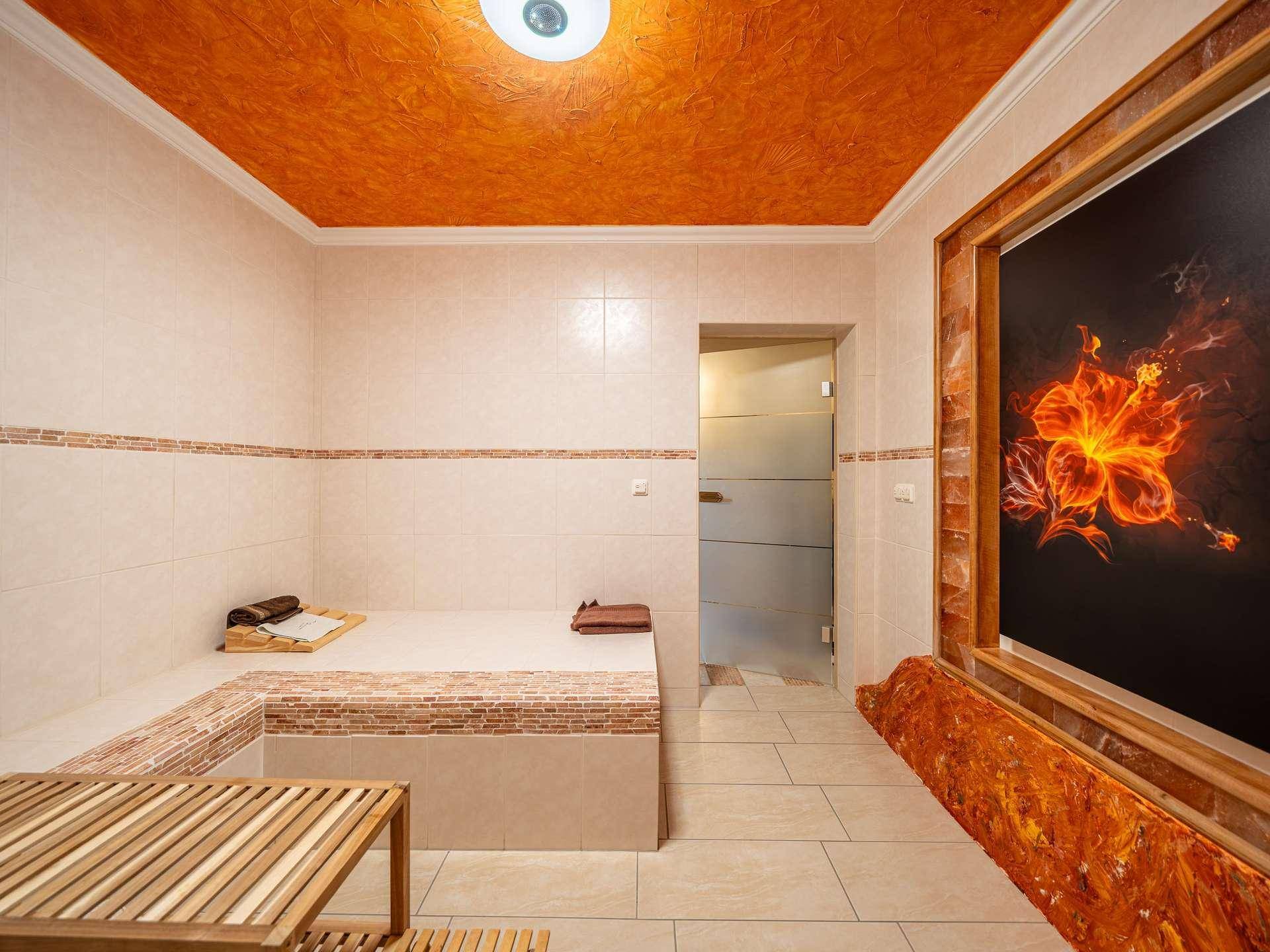 Wellnessbereich mit gefliesten Bänken, orangefarbener Decke und dekorativem Wandbild.