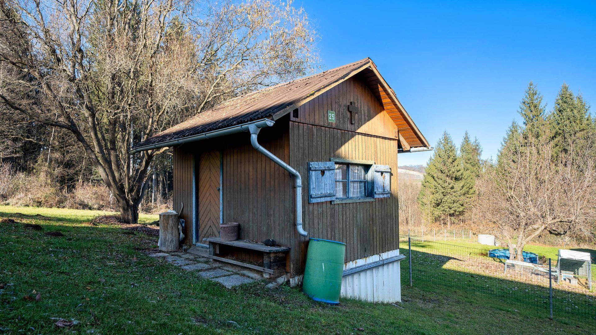 Rustikales Gartenhaus aus Holz in ländlicher Umgebung mit Blick auf Bäume.