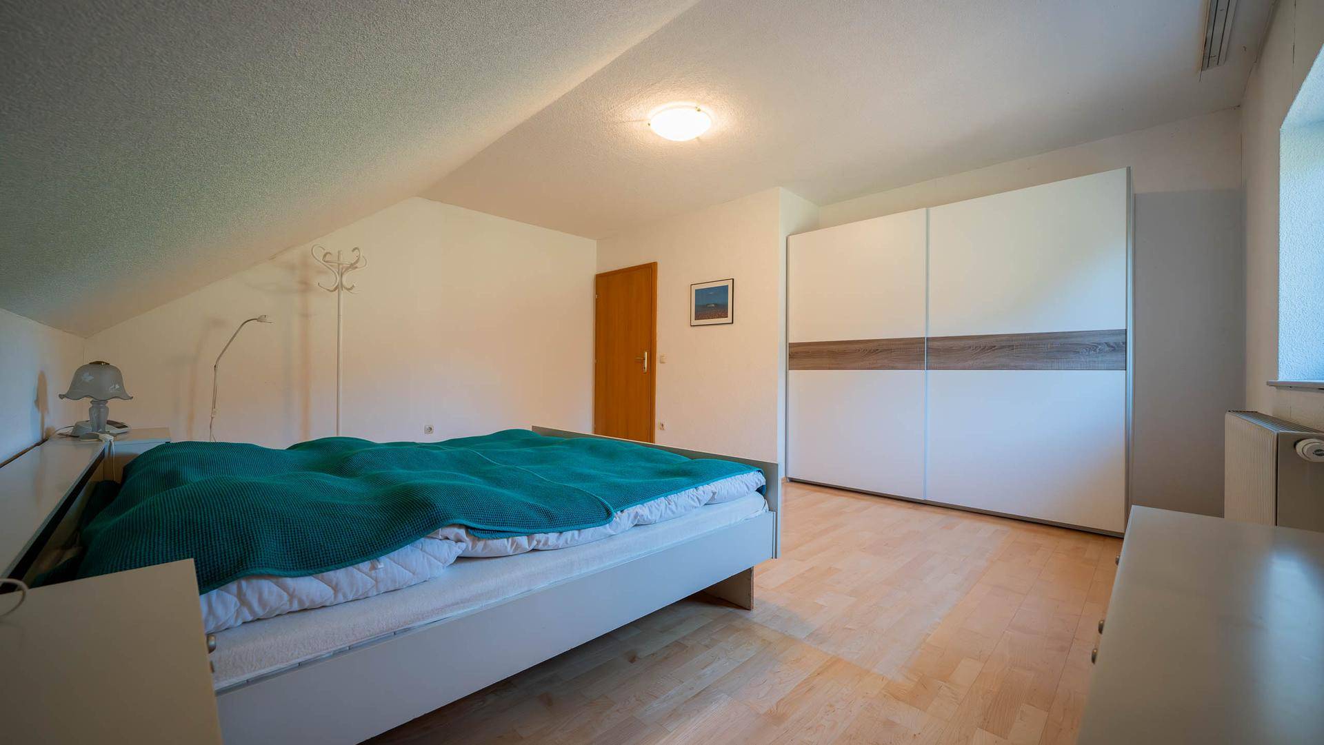 Schlafzimmer im Dachgeschoss mit Holzboden, Dachschräge und modernem Kleiderschrank.