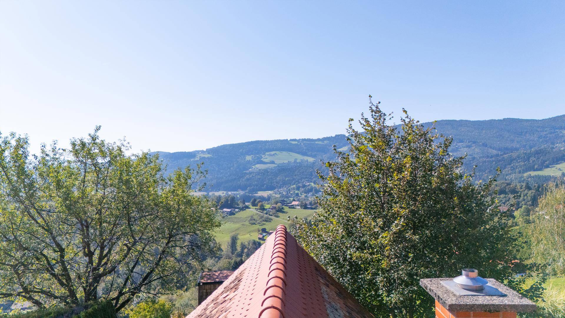 Ausblick über ein Ziegeldach auf die umliegenden grünen Hügel und Wälder.