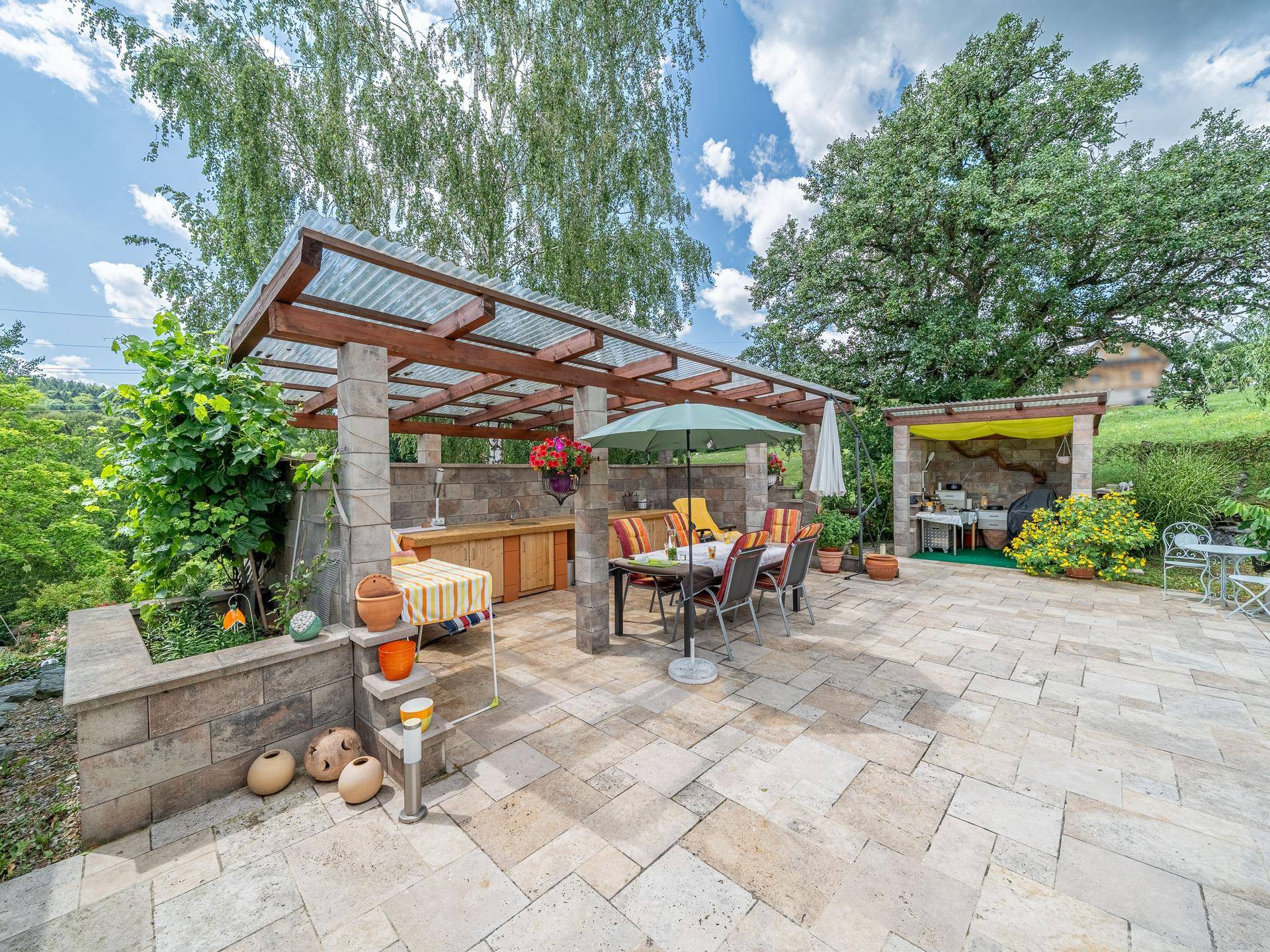 Großzügige, geflieste Terrasse mit überdachtem Essbereich und Außenküche, ideal für Unterhaltung.