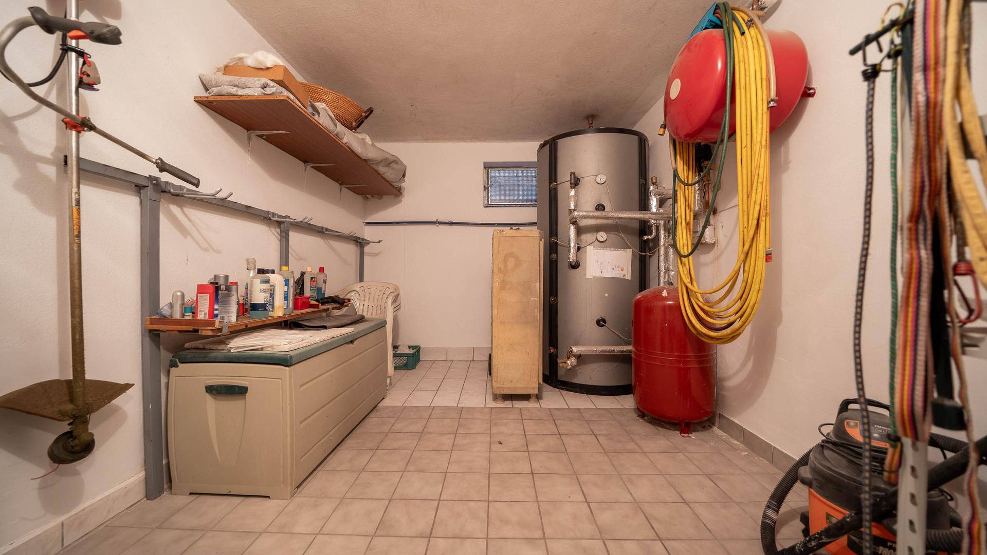 Technikraum im Keller mit Warmwasserspeicher, Heizungsanlage und Werkzeugen.