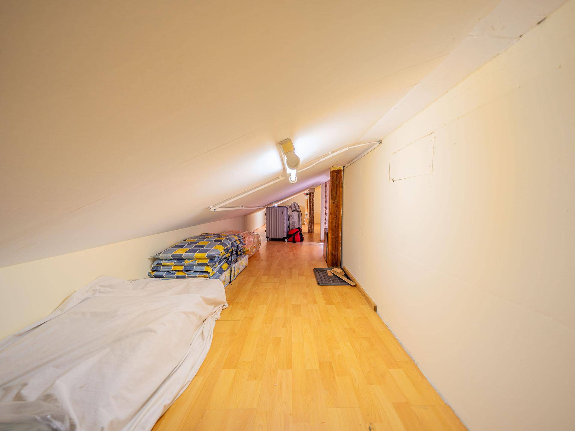 Dachboden mit schrägen Decken, Holzfußboden und Stauraum für verschiedene Gegenstände.