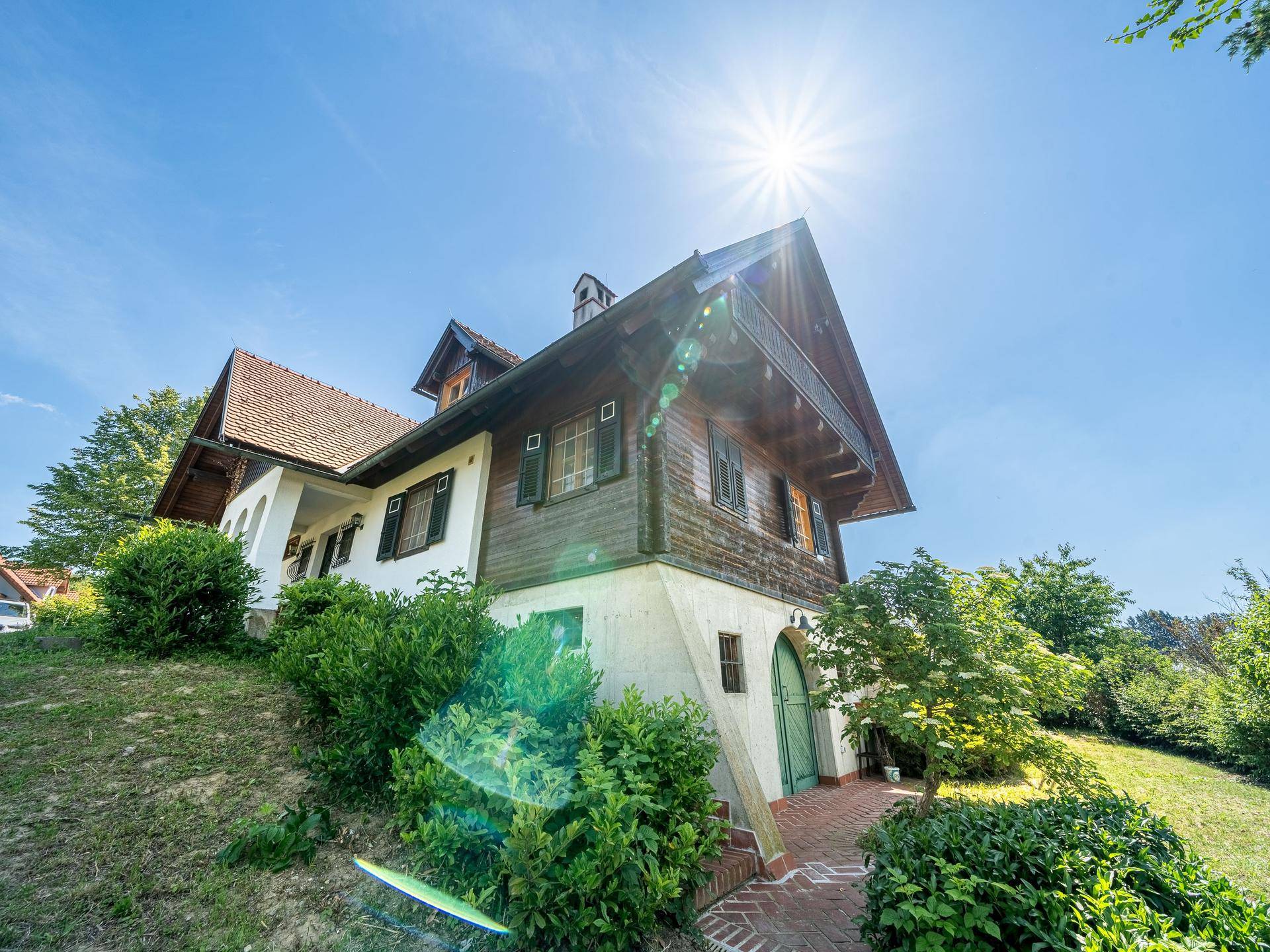 Sonniges Chalet-Haus auf einem Hanggrundstück mit traditioneller Architektur und grüner Bepflanzung.