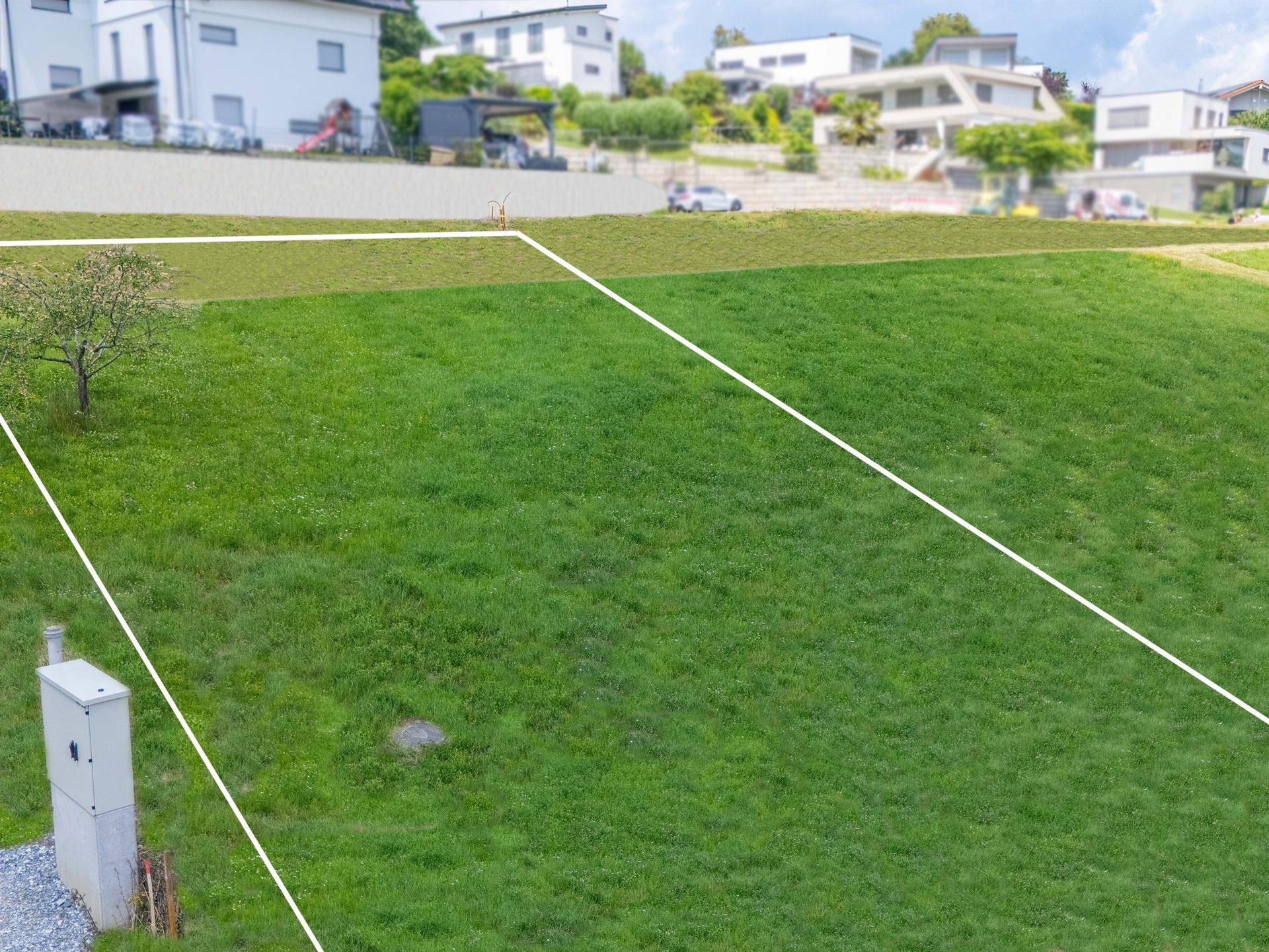 Luftaufnahme eines grünen Baugrundstücks mit markierten Grenzen und modernen Häusern in der Umgebung.
