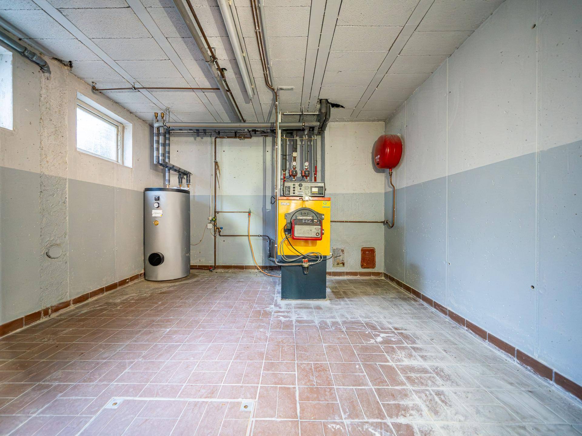 Heizungsraum im Keller mit Warmwasserbereiter, Heizkessel und robustem Fliesenboden.