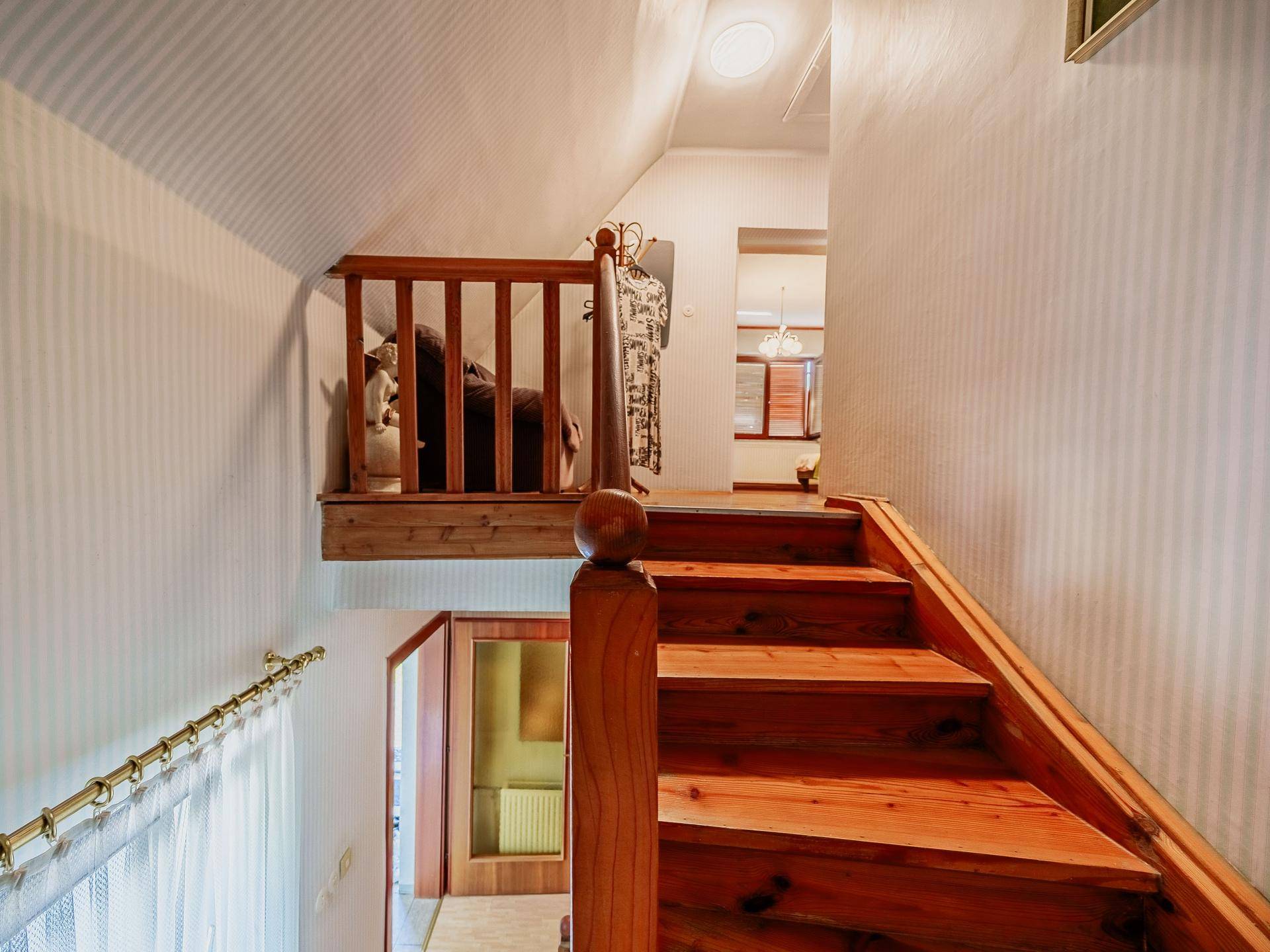 Holztreppe führt in das obere Stockwerk, mit hellem Geländer und gestreiften Tapeten.
