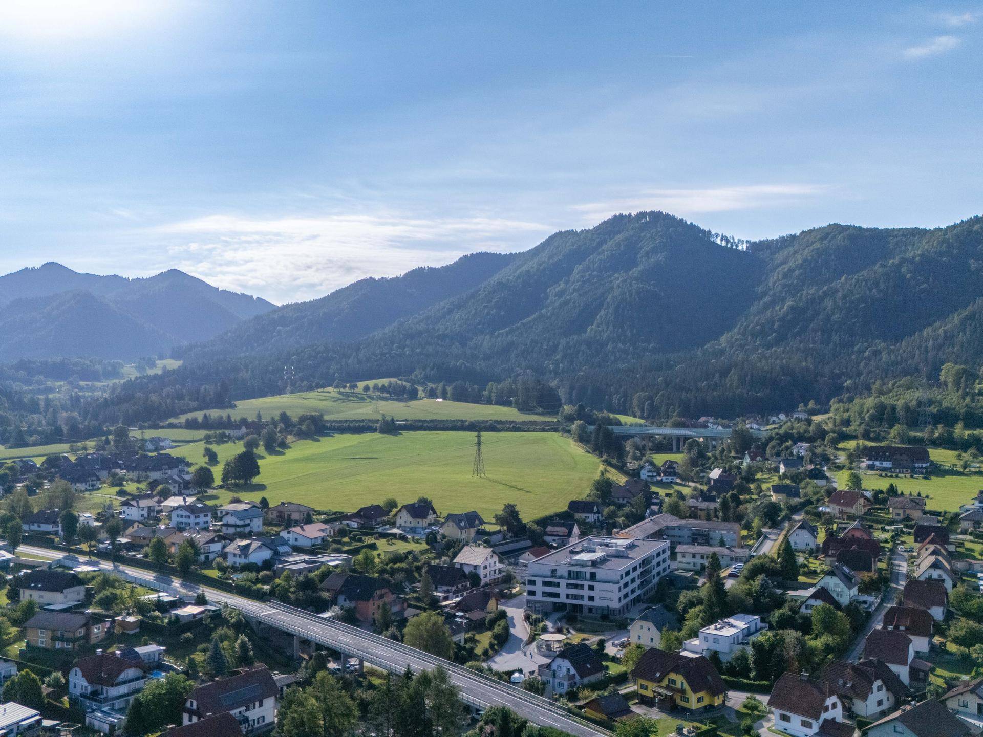 Panoramablick über eine malerische Stadt in einem Tal, umgeben von weiten Feldern und majestätischen Bergen.